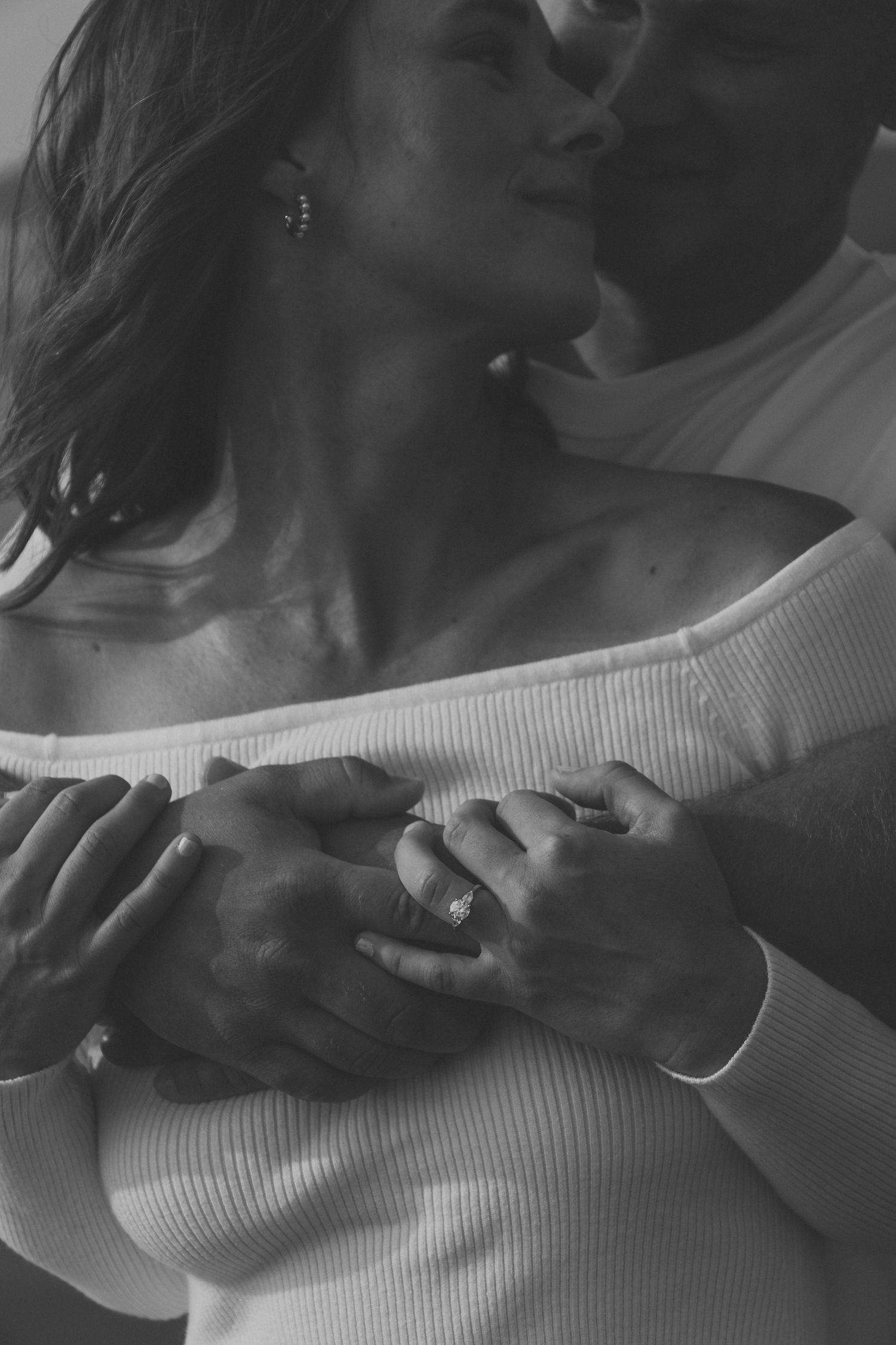 Black and white romantic couple embracing, woman wearing engagement ring and off-shoulder white top.