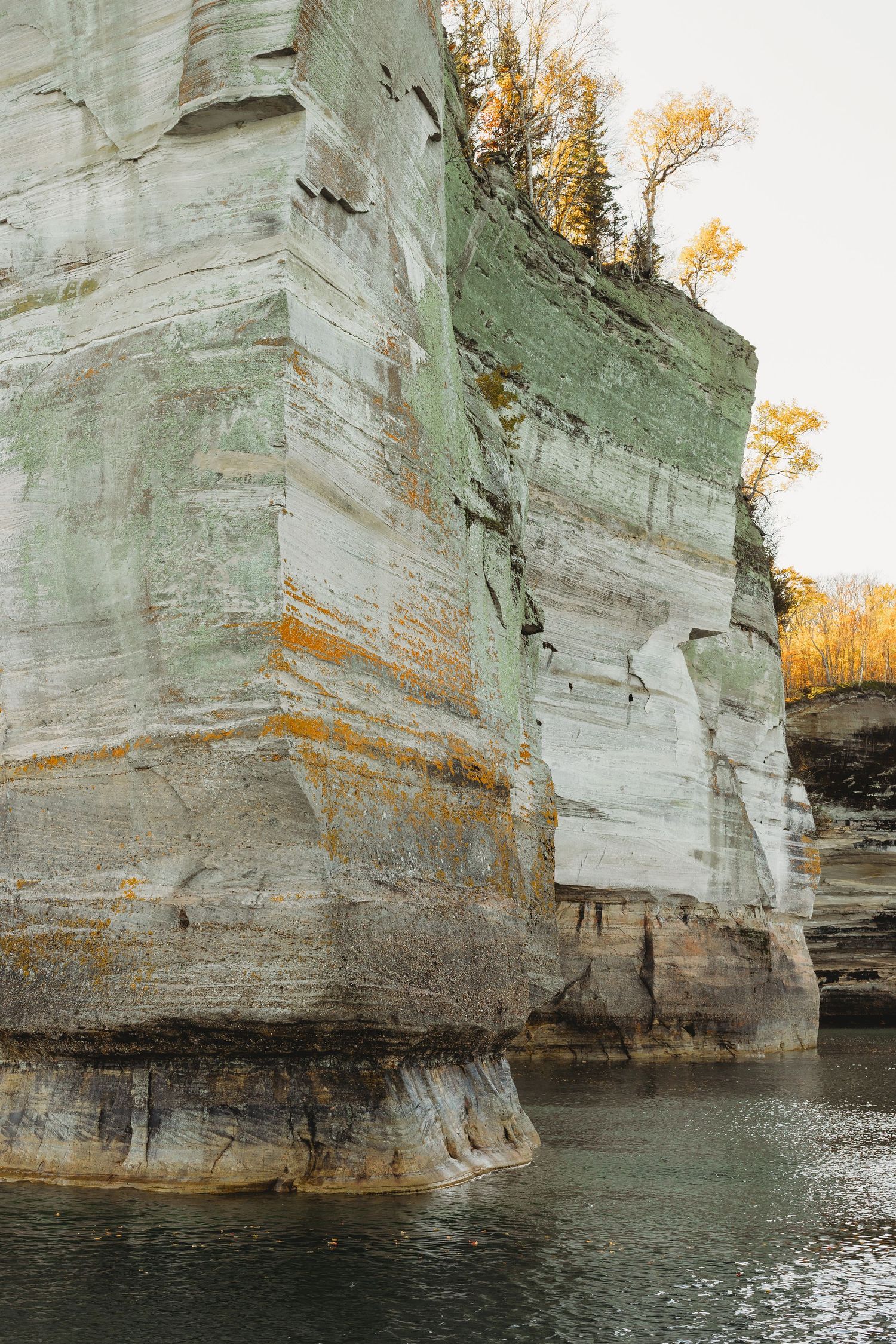 Towering limestone cliffs rising from clear water with autumn trees on top.