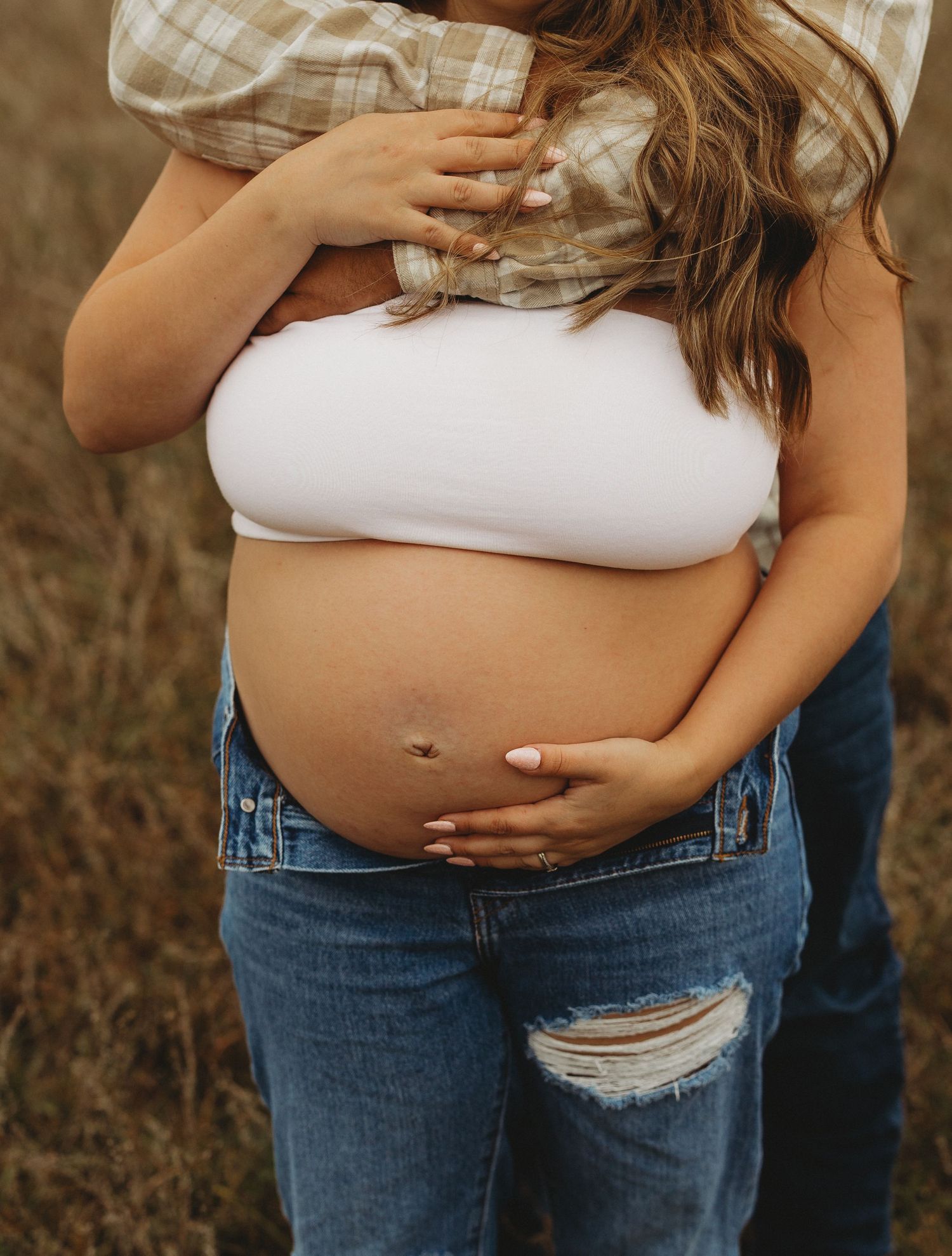 Maternity photo showing pregnant belly with hands lovingly placed on bump, wearing casual denim.