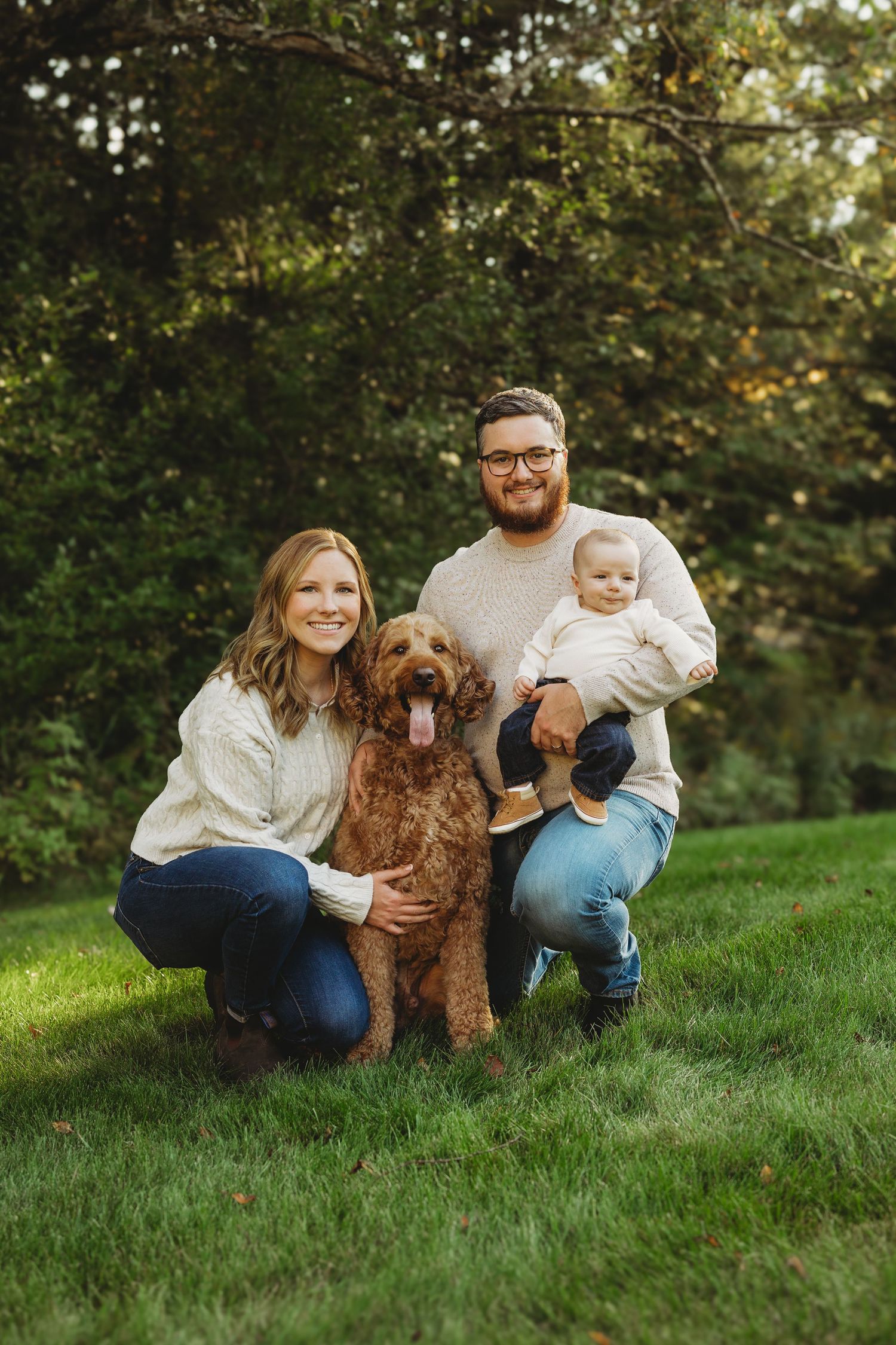 Family sitting on grassy hill with their goldendoodle dog during an outdoor photo session.