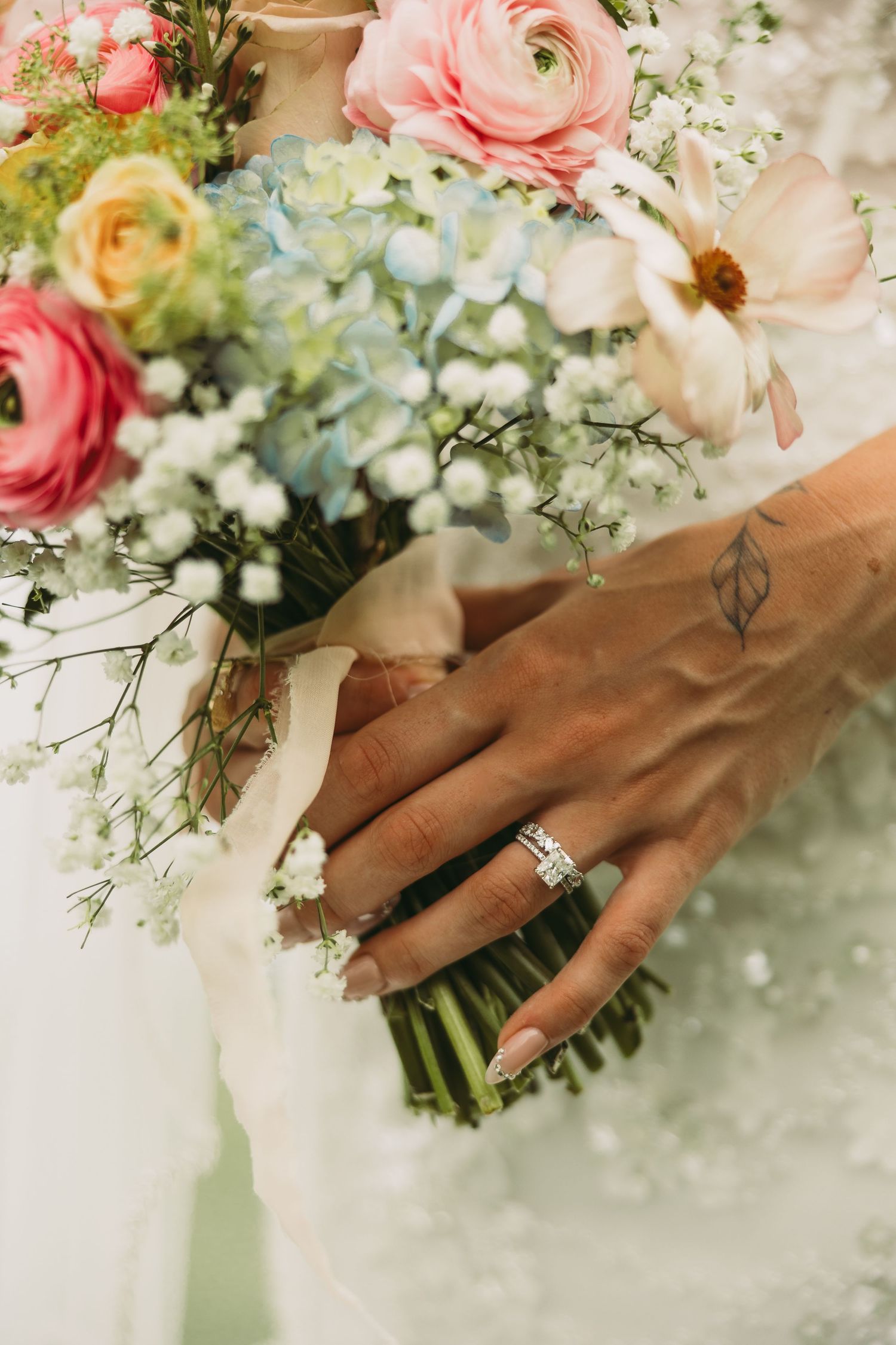 Close-up of a bridal bouquet with pink and yellow roses, with an engagement ring visible on the hand.