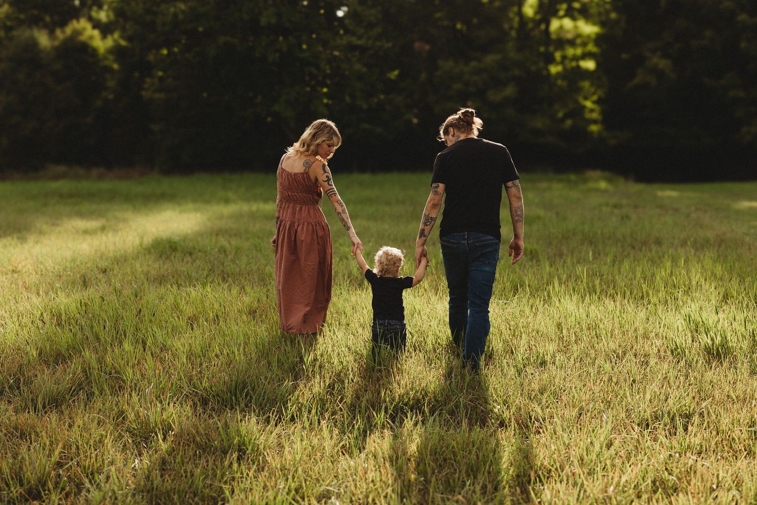 A family walks hand in hand through a sun-drenched meadow during golden hour.