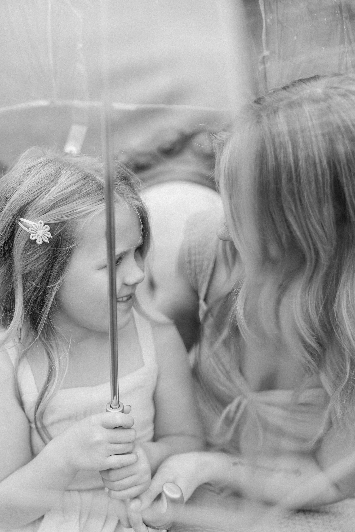 Black and white photo of a mother and young daughter sharing a tender moment under a clear umbrella.