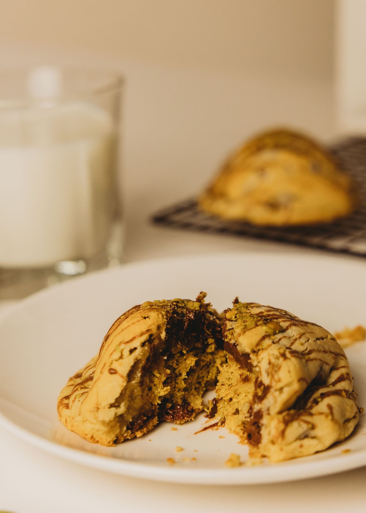 Close-up of a broken matcha chocolate chip cookie on a white plate with a glass of milk in the background.