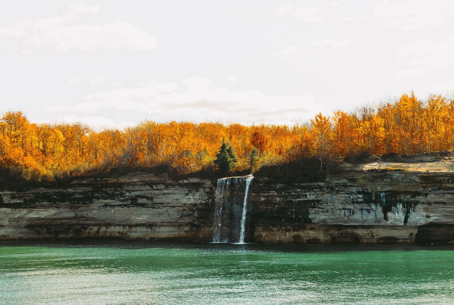 Scenic waterfall cascading over limestone cliffs with autumn foliage in the background.