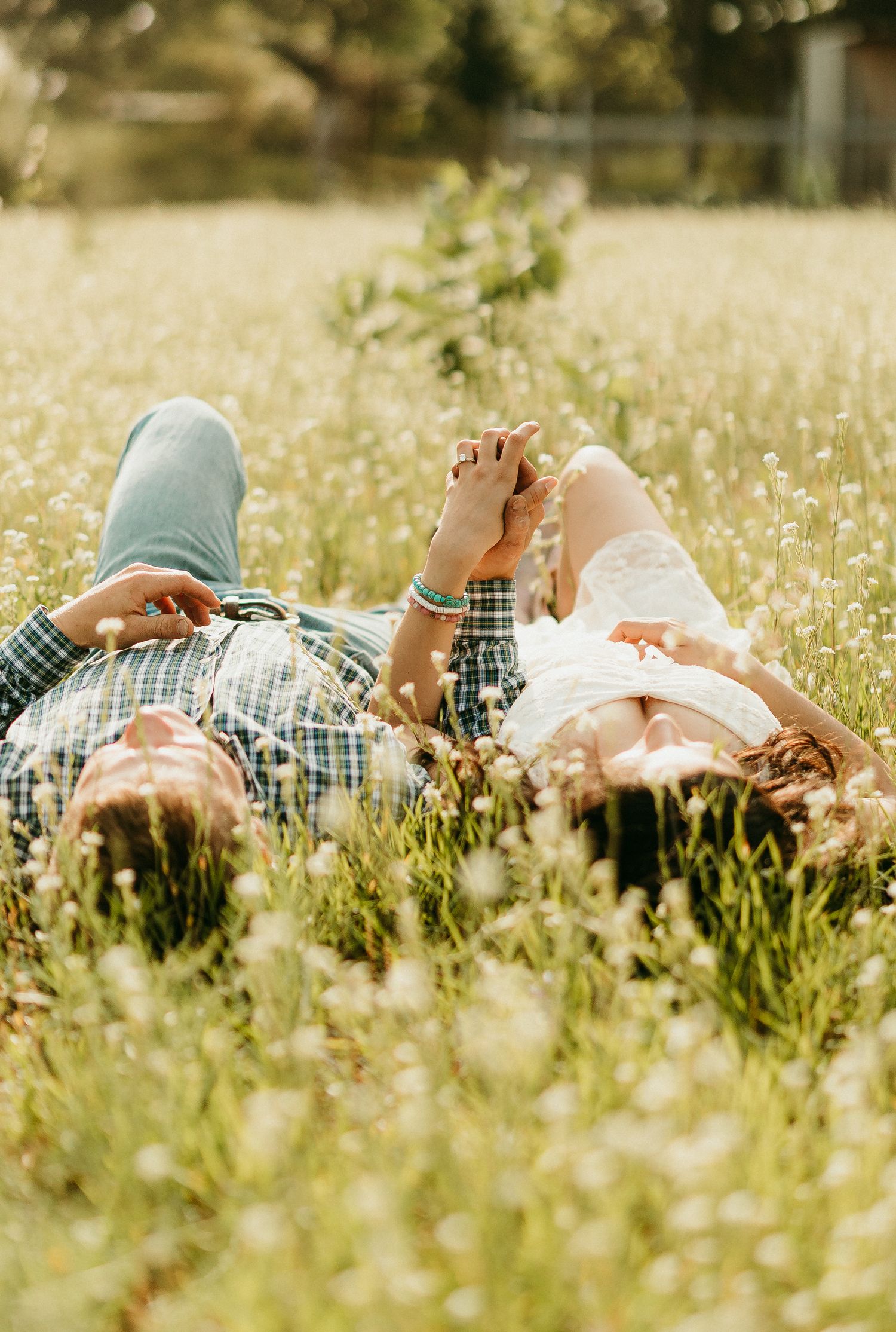 A couple lying in a sunny meadow filled with white wildflowers on a warm summer day.