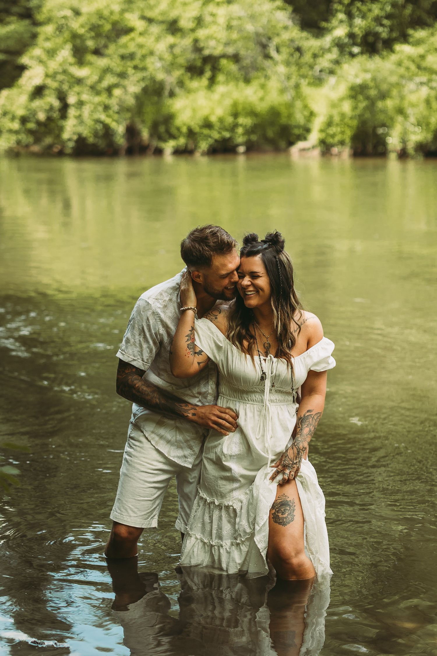 Couple in matching white outfits embracing while standing in river water.