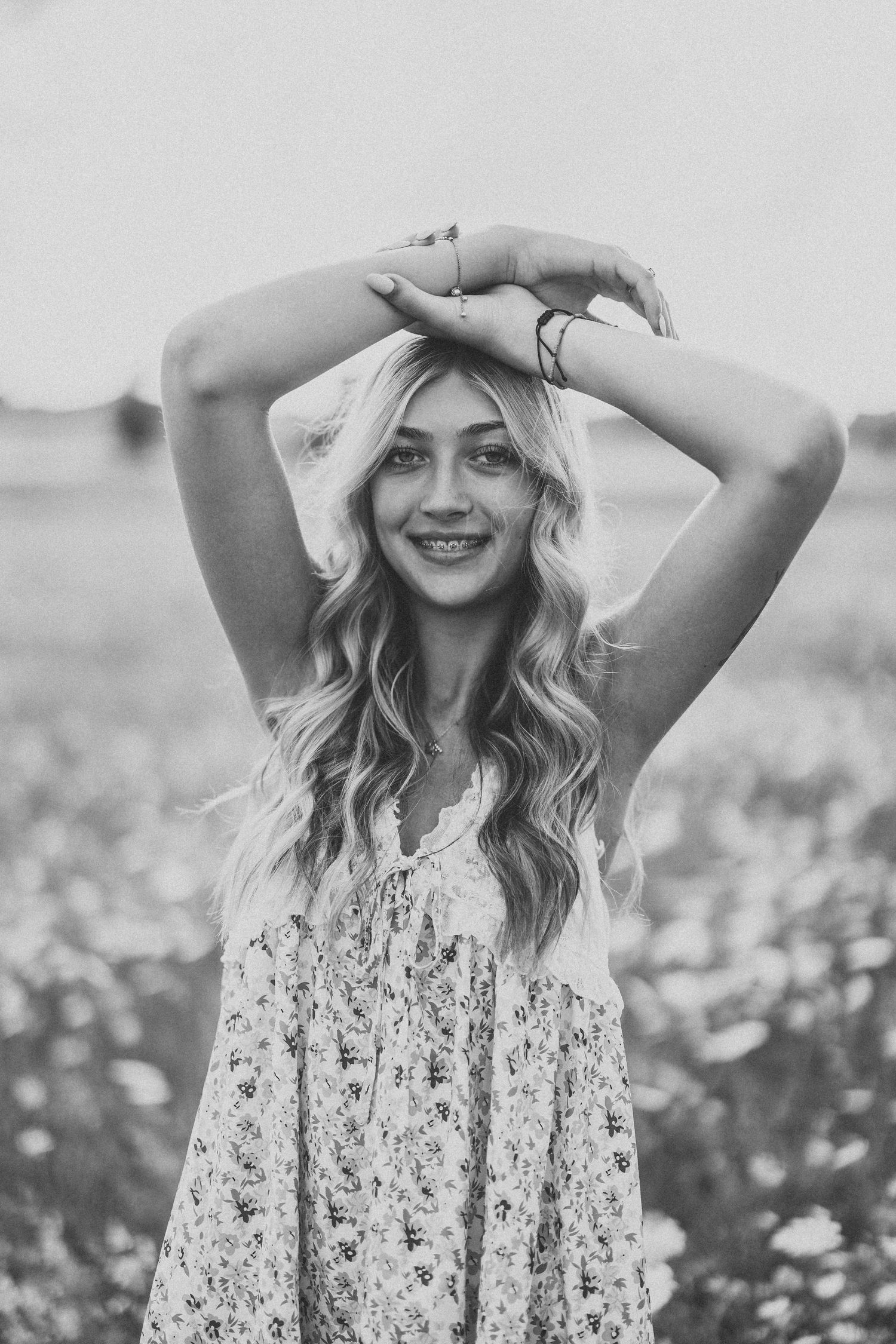 Black and white portrait of someone posing playfully in a floral dress outdoors.