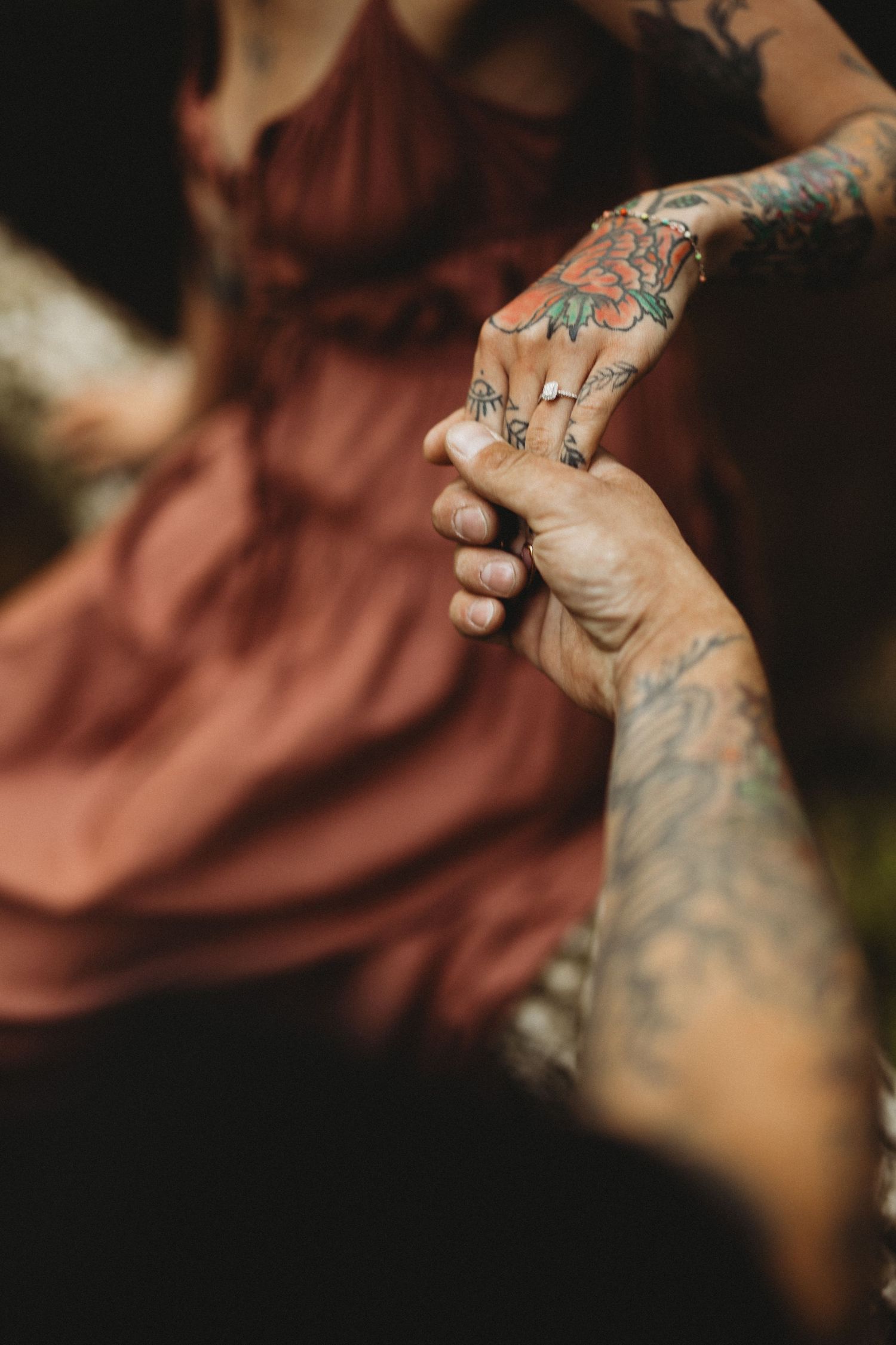 Close-up of tattooed hands with multiple rings in a dark, artistic setting.