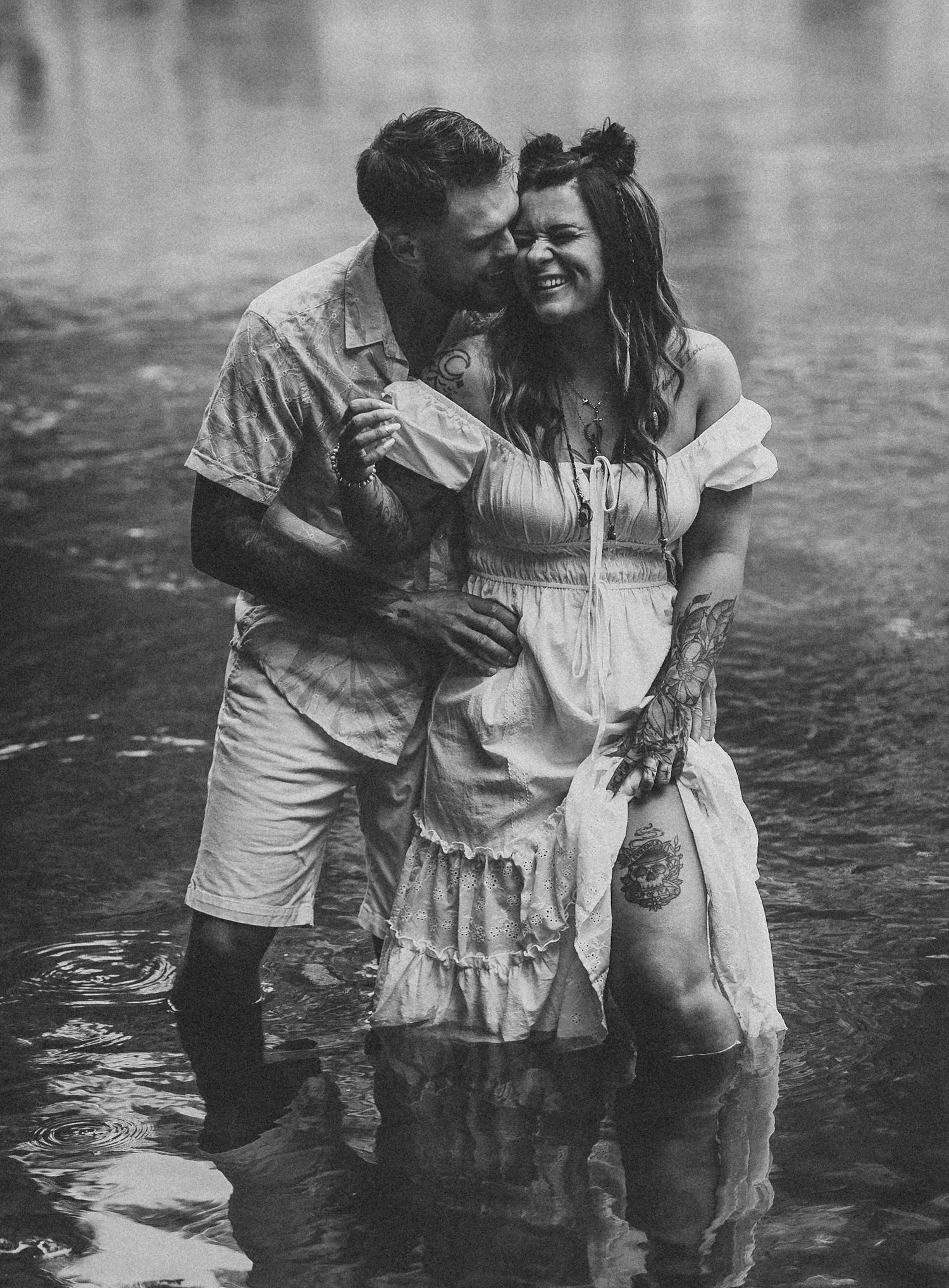 Couple playing and laughing together in shallow water wearing white clothes.