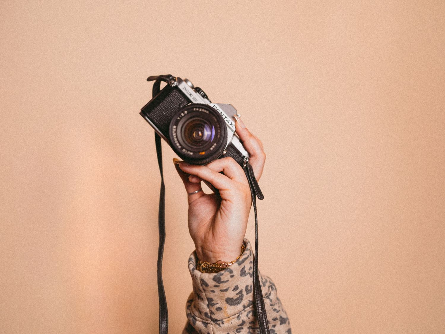 Tattooed hands holding vintage camera against peach background.