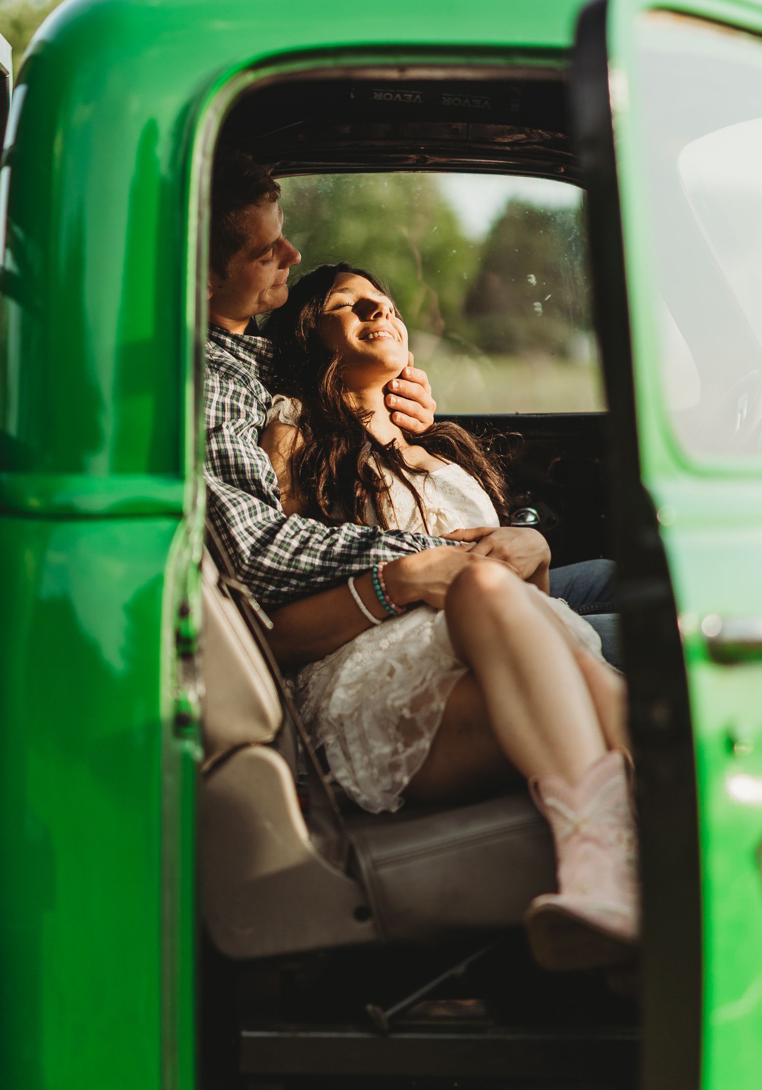 Couple sharing intimate moments inside a green vintage vehicle during golden hour sunlight.