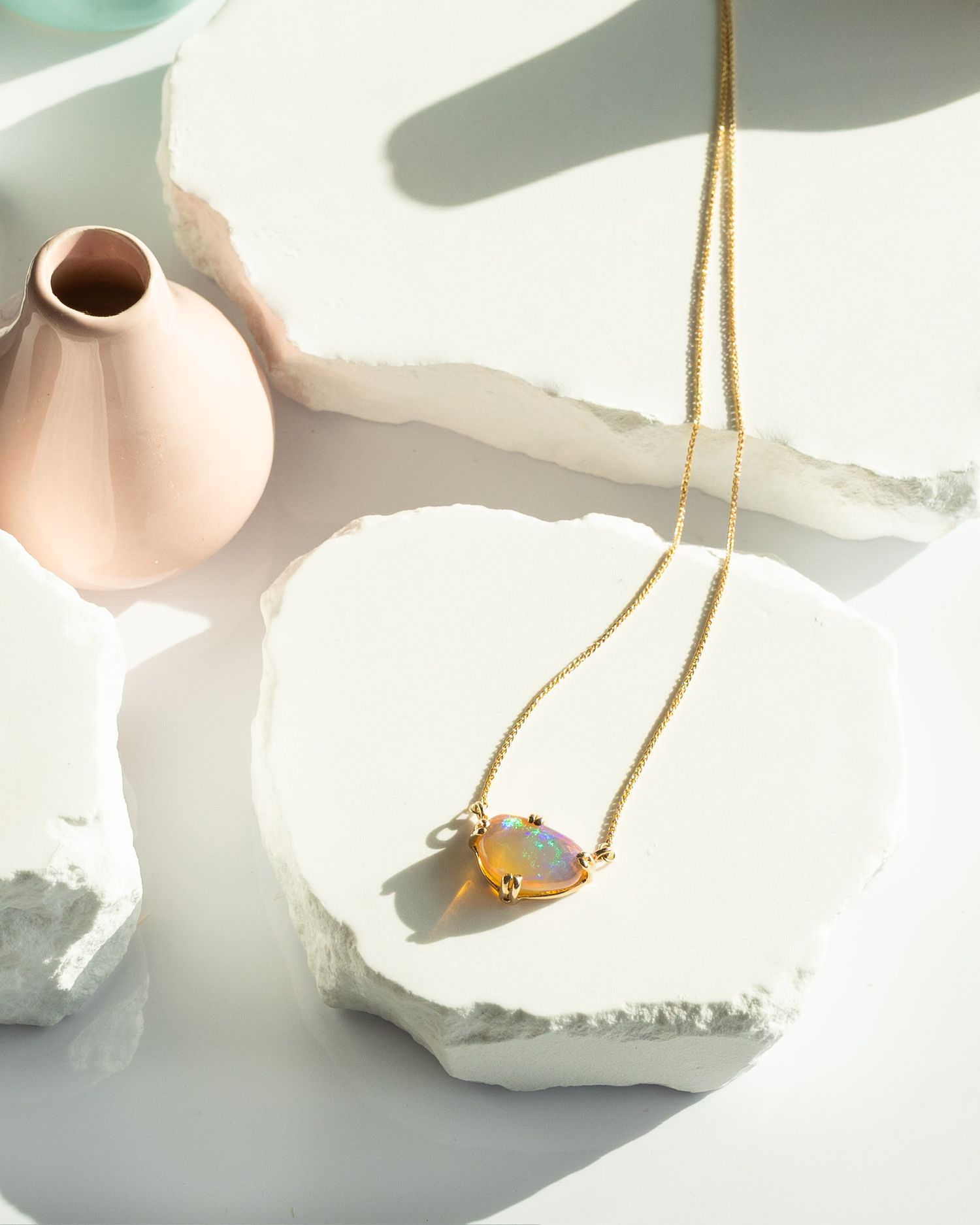 Minimalist still life with gold necklace casting shadows on white surface.