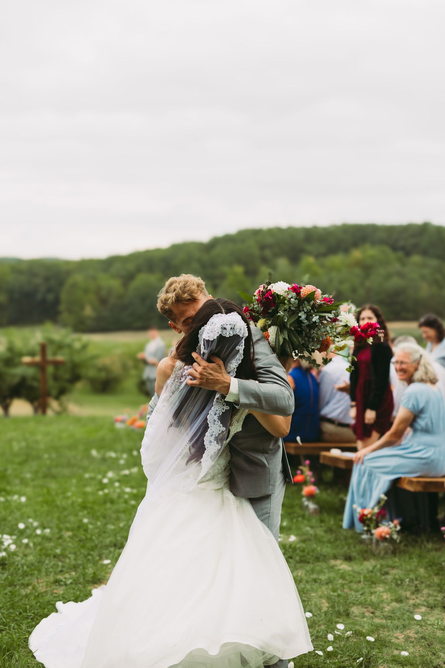 A couple celebrates during their outdoor wedding ceremony in a scenic field with rolling hills.