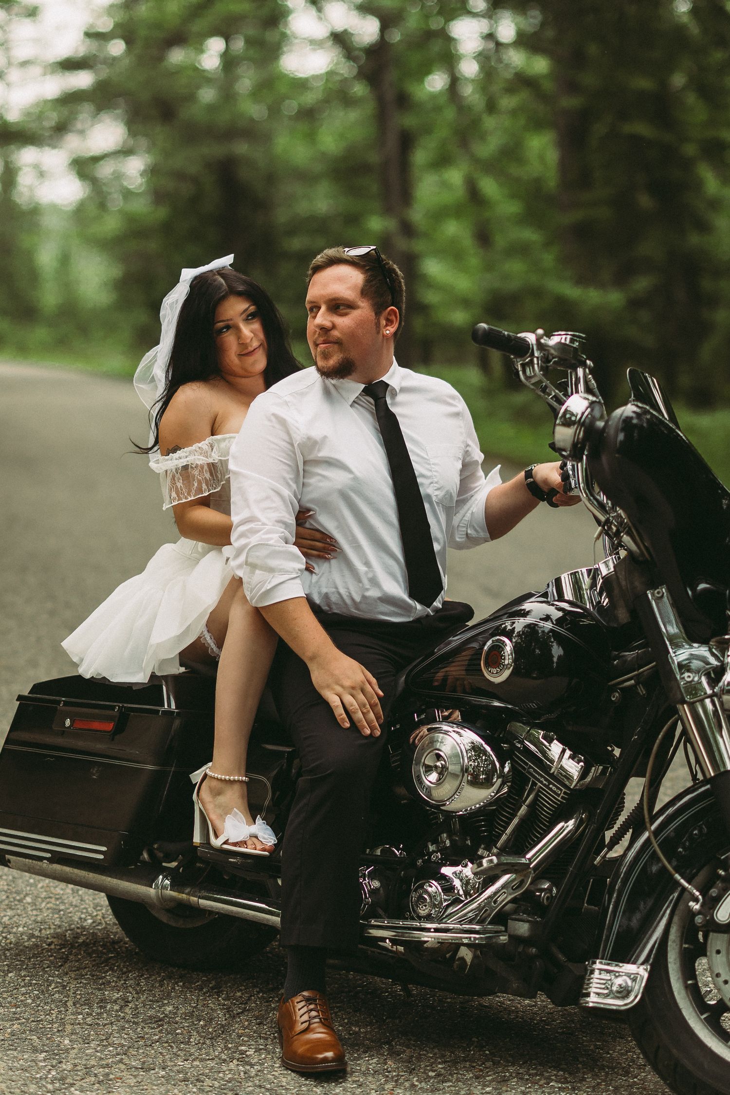 Romantic motorcycle photoshoot featuring a black Harley-Davidson cruiser on a forest road.