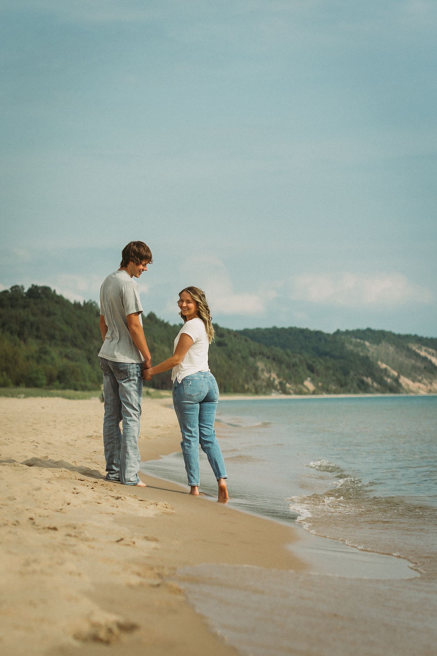 Two people walking along the shoreline of a scenic beach with cliffs in the background.