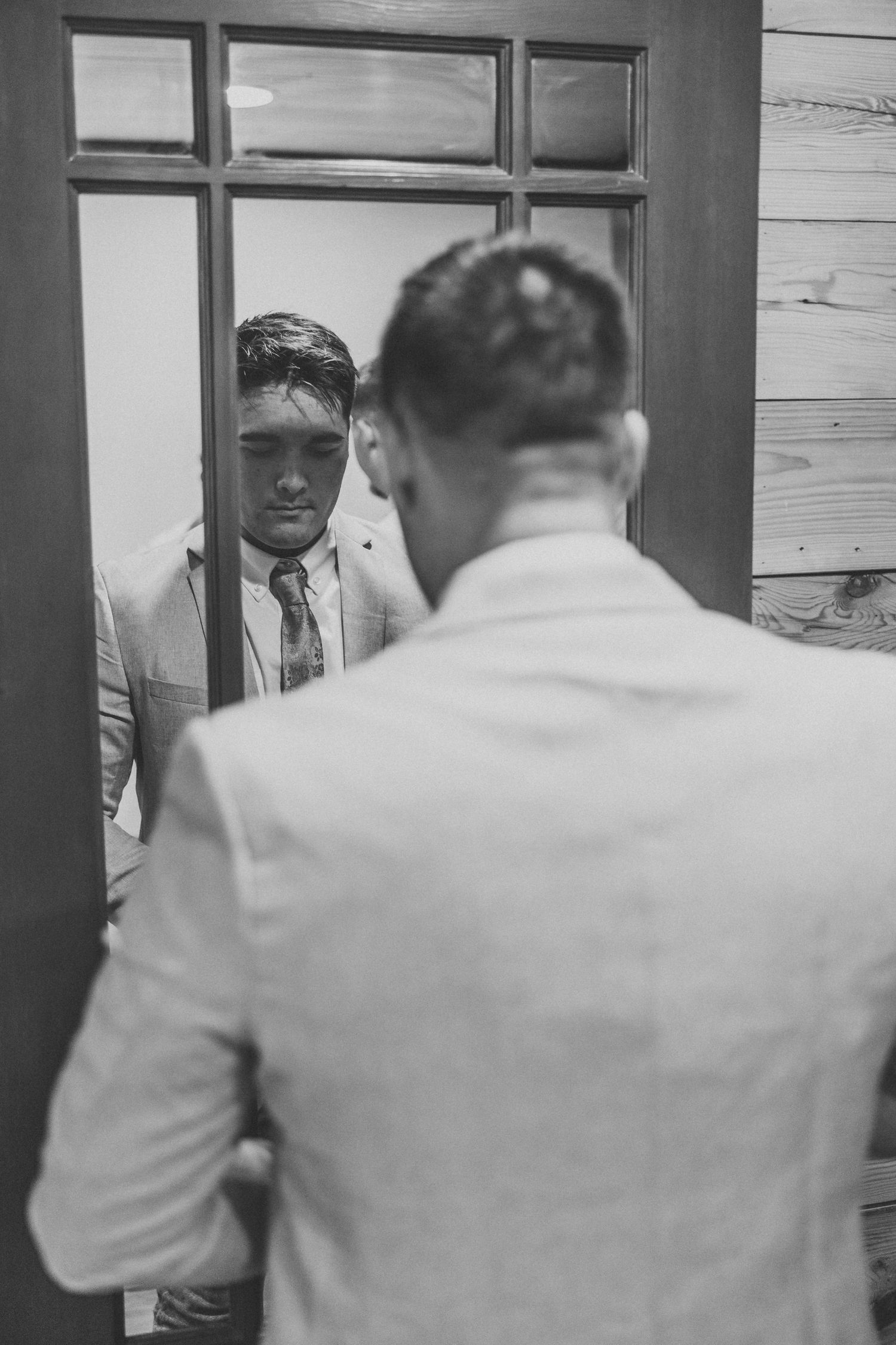 Black and white sequence of a groom getting ready in front of a mirror.