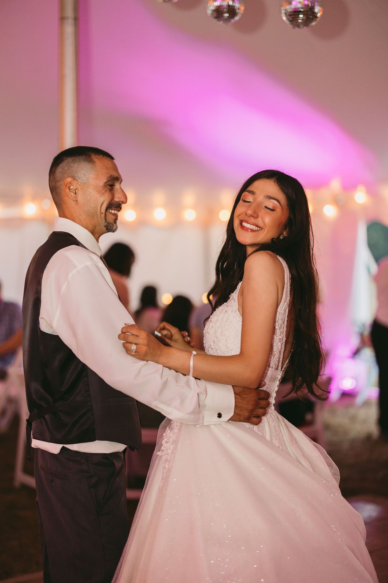 Couple sharing a joyful dance moment under pink lighting at their wedding reception.