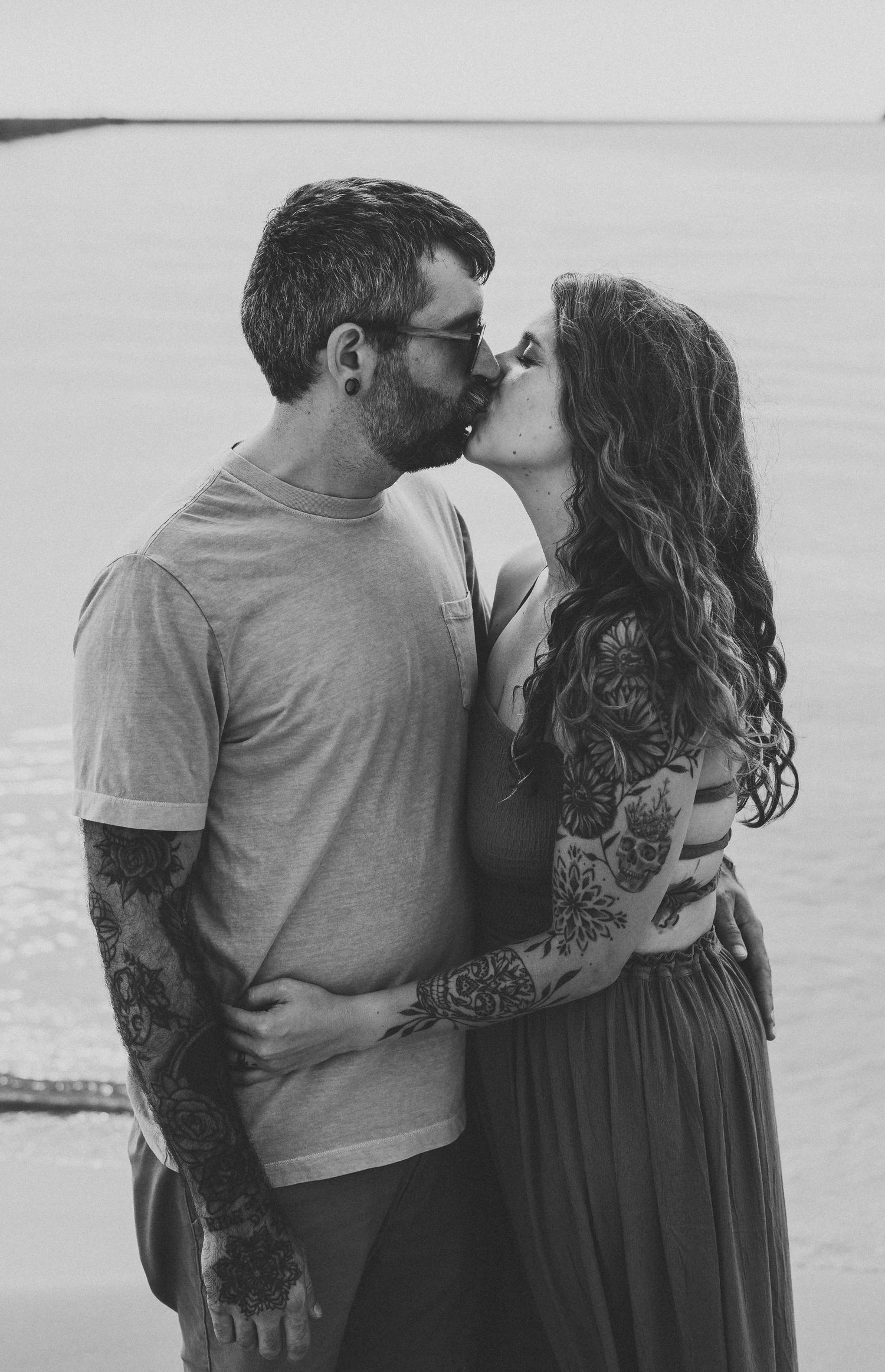A romantic black and white photo series showing a couple embracing on the beach in casual attire.