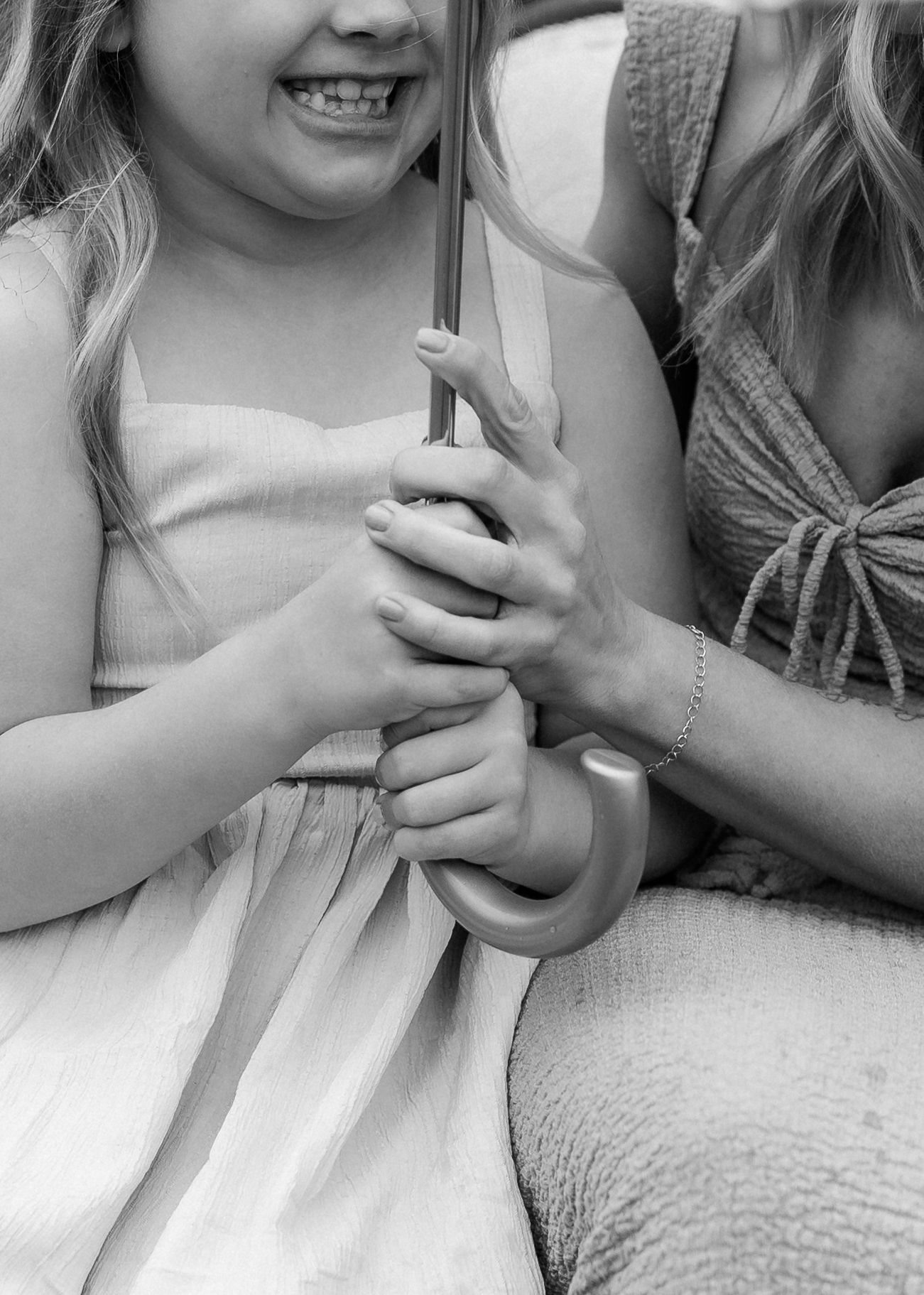 Black and white photo of a mother and young girl holding an umbrella together, sharing a joyful moment.