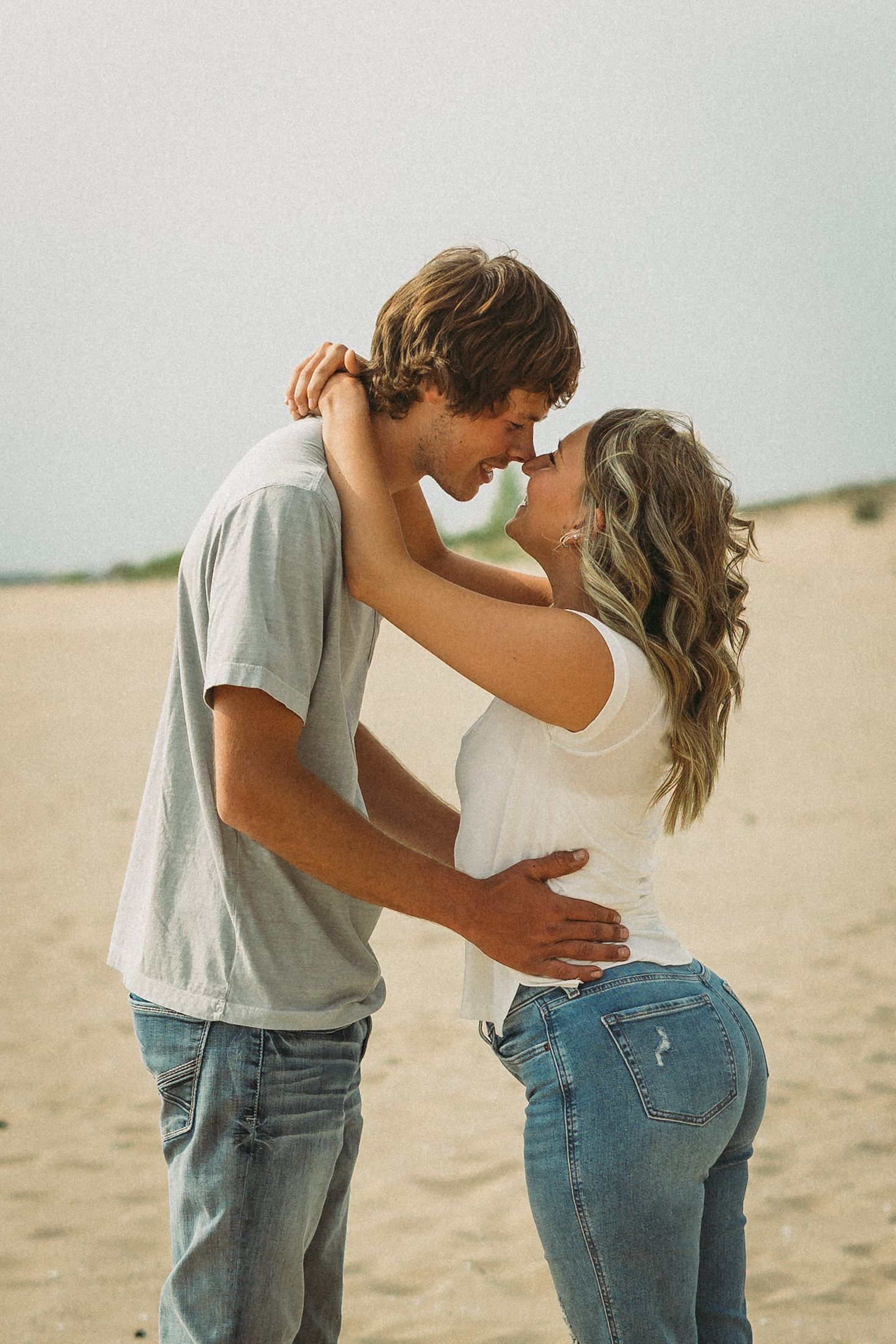 Candid beach photography capturing intimate moments between a couple in casual denim and t-shirts.