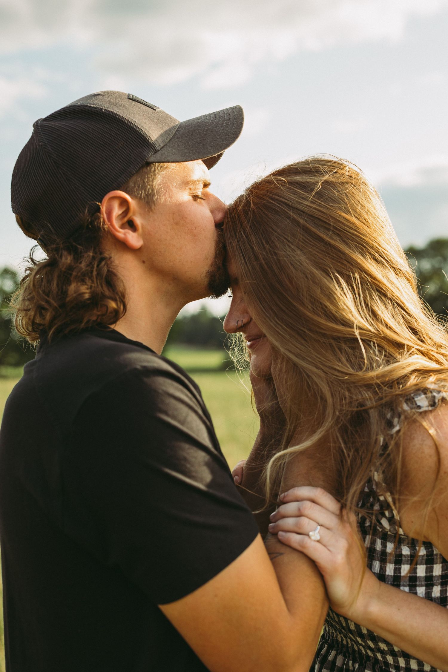 Couple sharing intimate moments in sunlit field wearing casual attire.