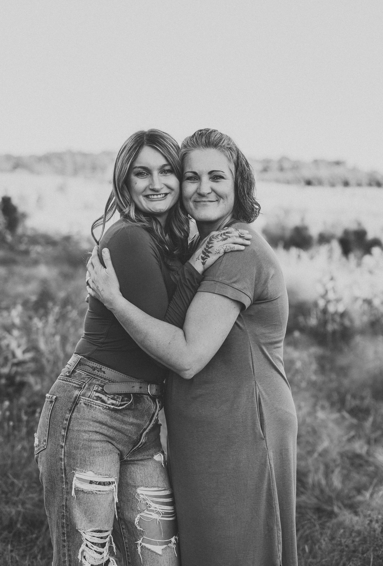 Two women embracing and smiling in black and white outdoor portrait.