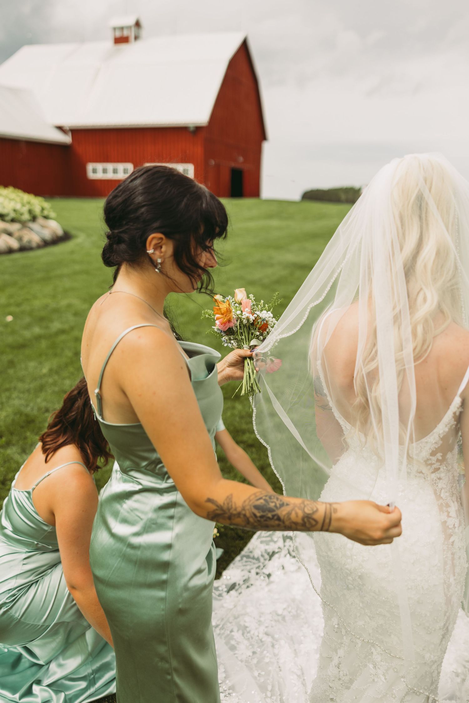 Wedding party members in mint dresses help adjust bridal veil outdoors.