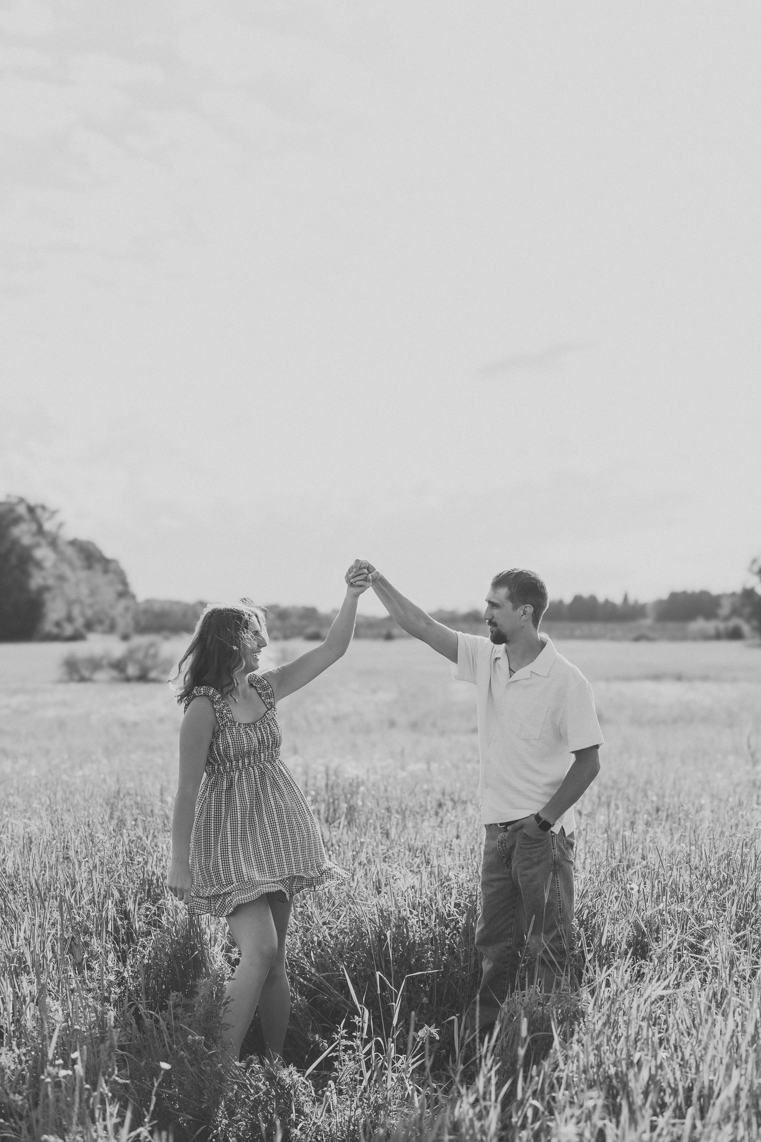 Black and white photo of a couple dancing in a field, man spinning woman while holding hands outdoors.
