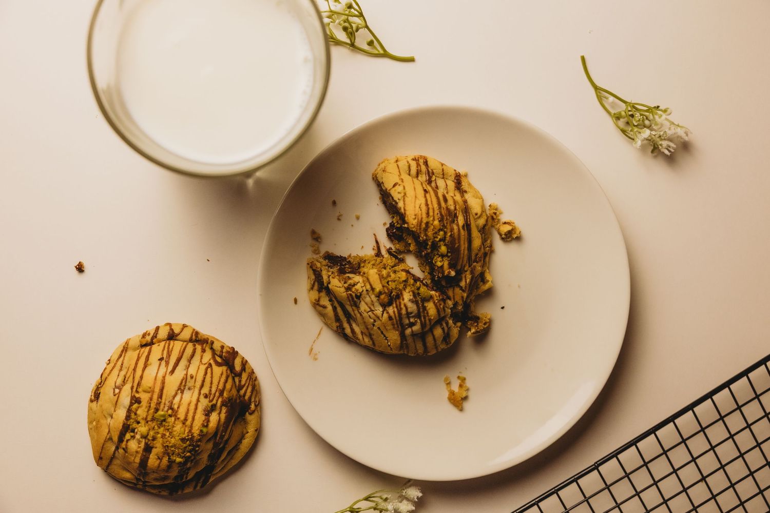 Overhead view of chocolate drizzled cookies on a white plate with a glass of milk and dried flowers.