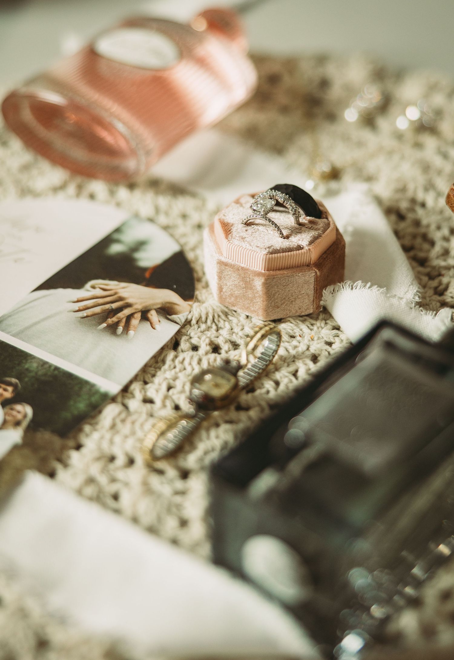 Vintage photographs and a pink ring box displayed on delicate lace with decorative shell accessories in soft lighting.