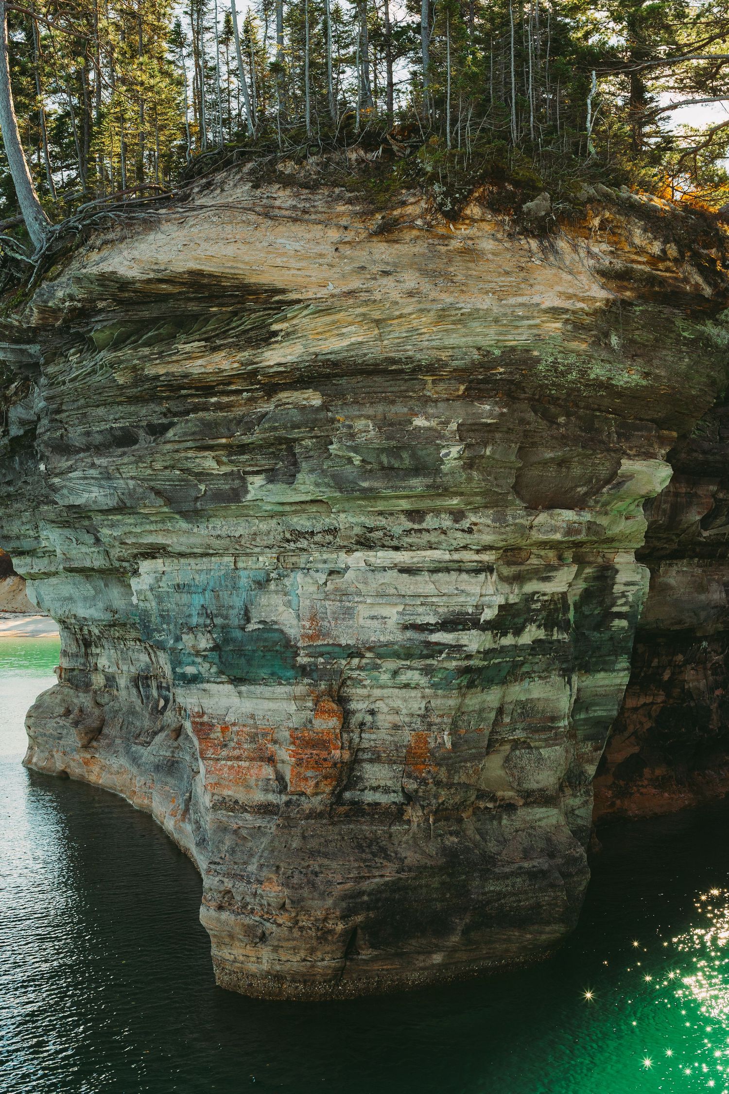 Layered rock formations of Pictured Rocks National Lakeshore with emerald waters below.