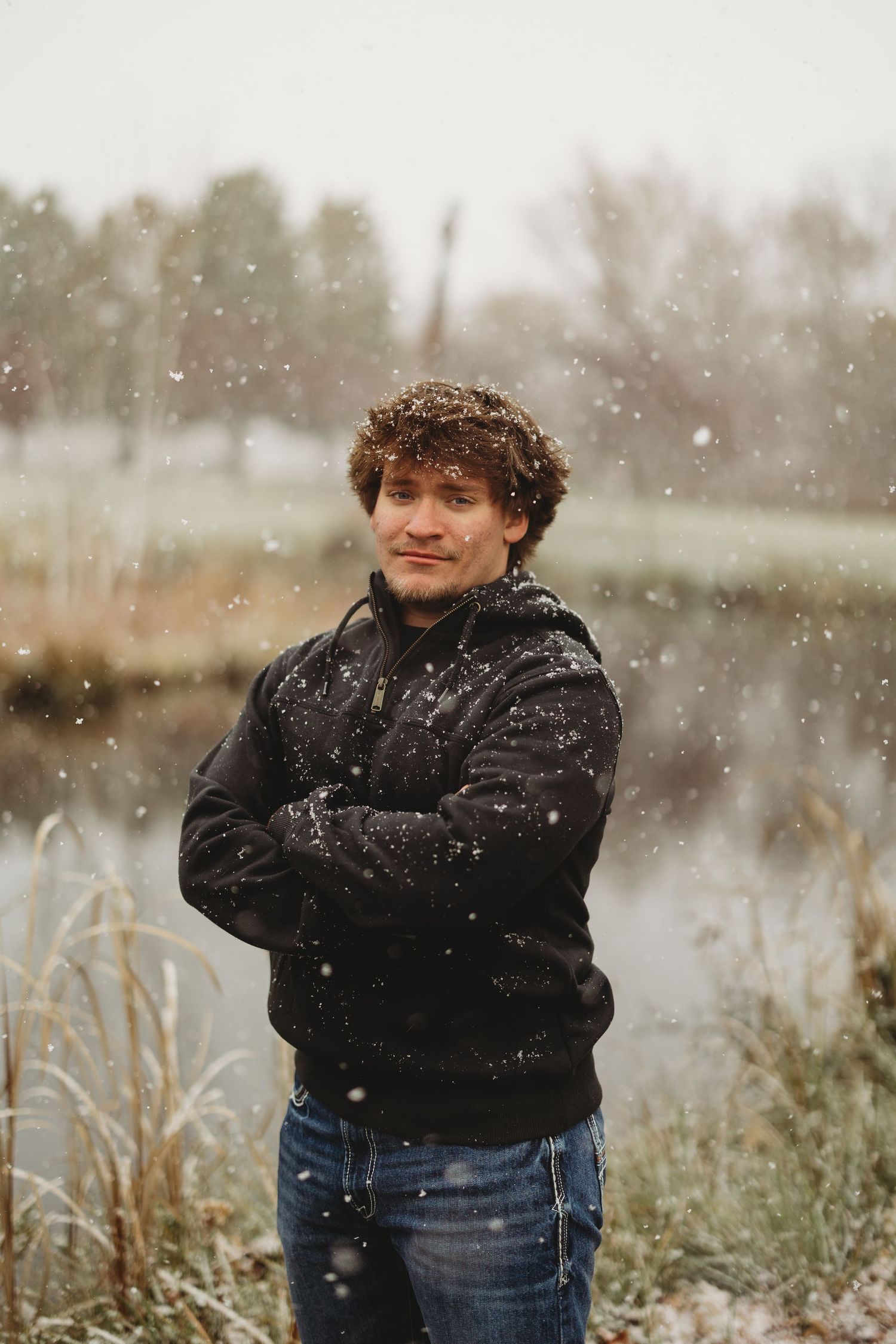 Person in black hoodie standing outdoors while snow falls.