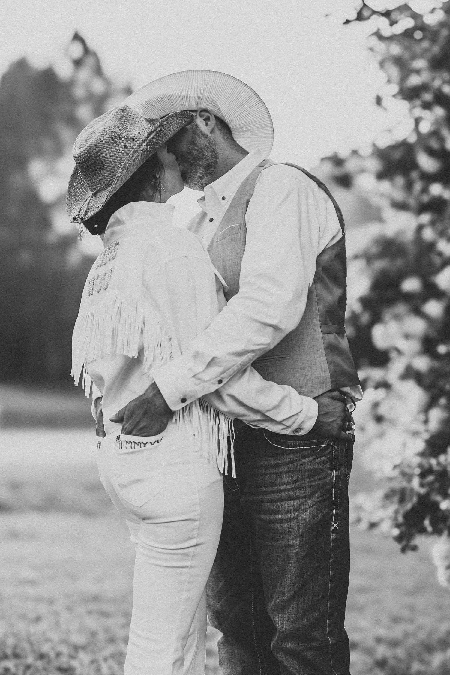 Black and white photo of a couple in western wear embracing in a field.