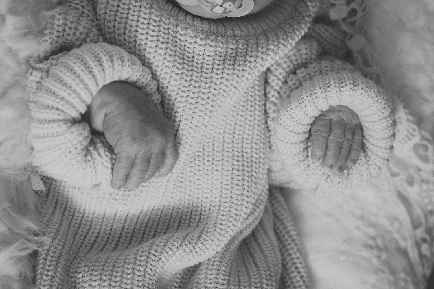 Newborn baby wrapped in cozy gray knit sweater on white blanket.