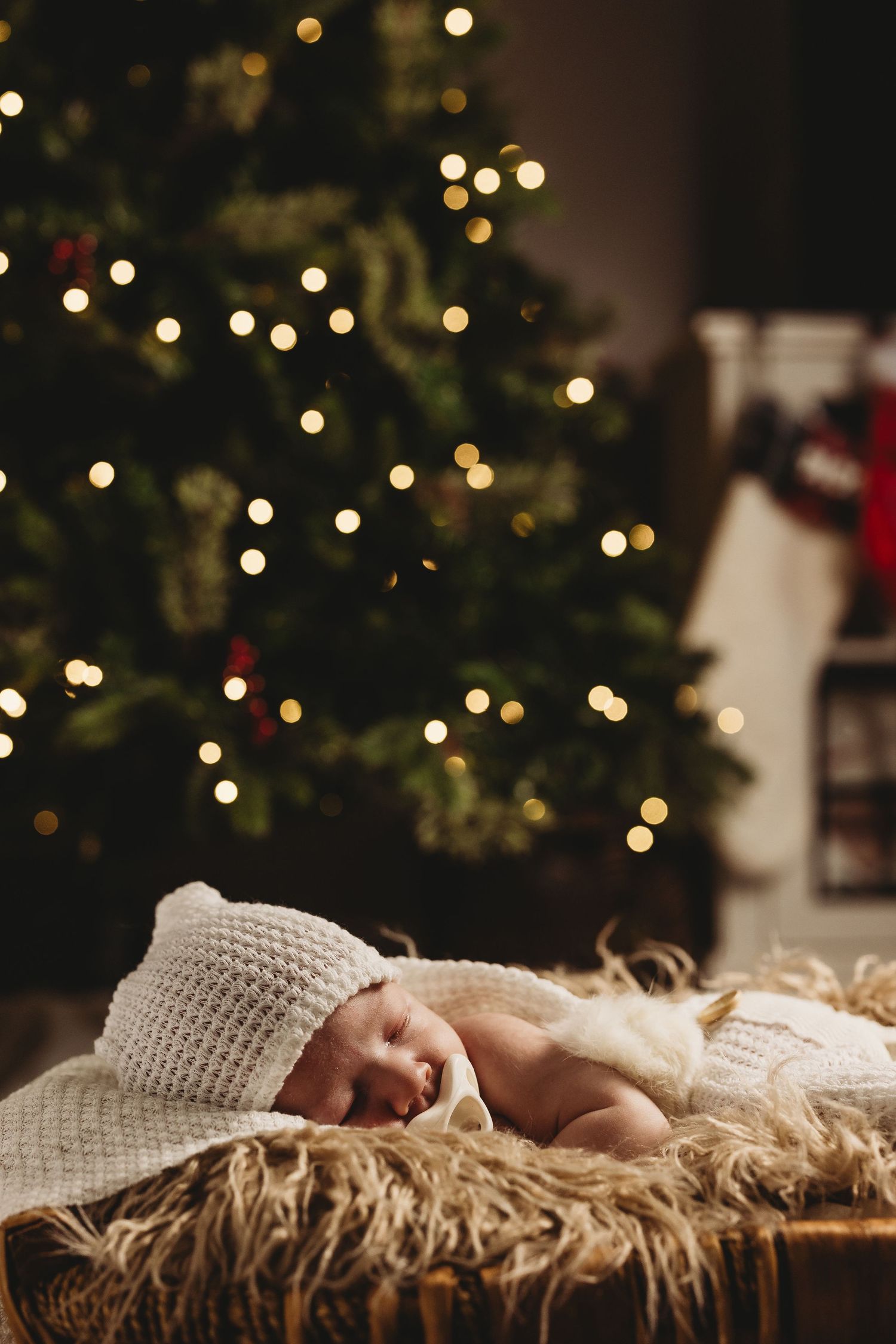Baby sleeping on fur blanket with bokeh Christmas lights creating magical holiday ambiance.