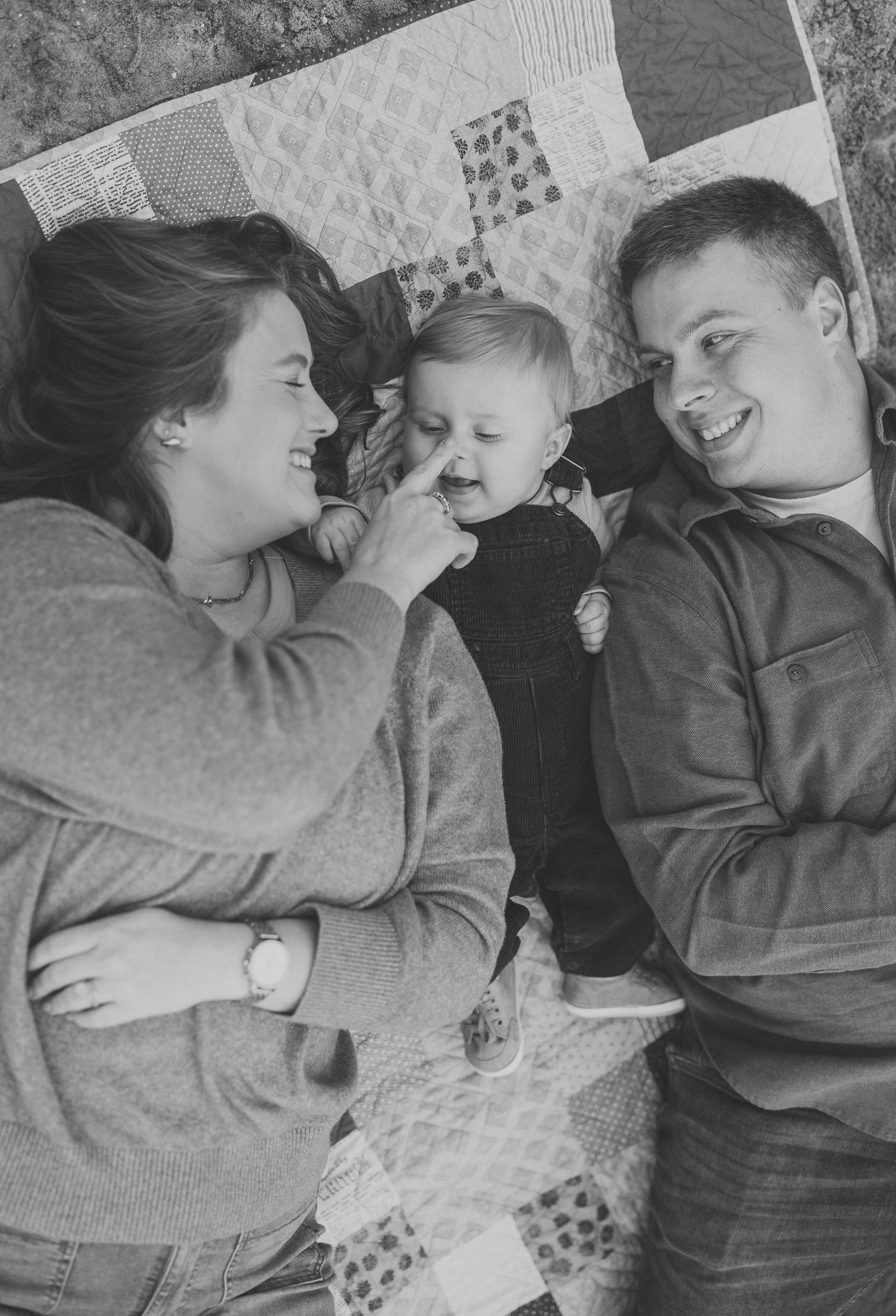 A vintage black and white photo of a family sharing a joyful moment together on a patterned quilt.