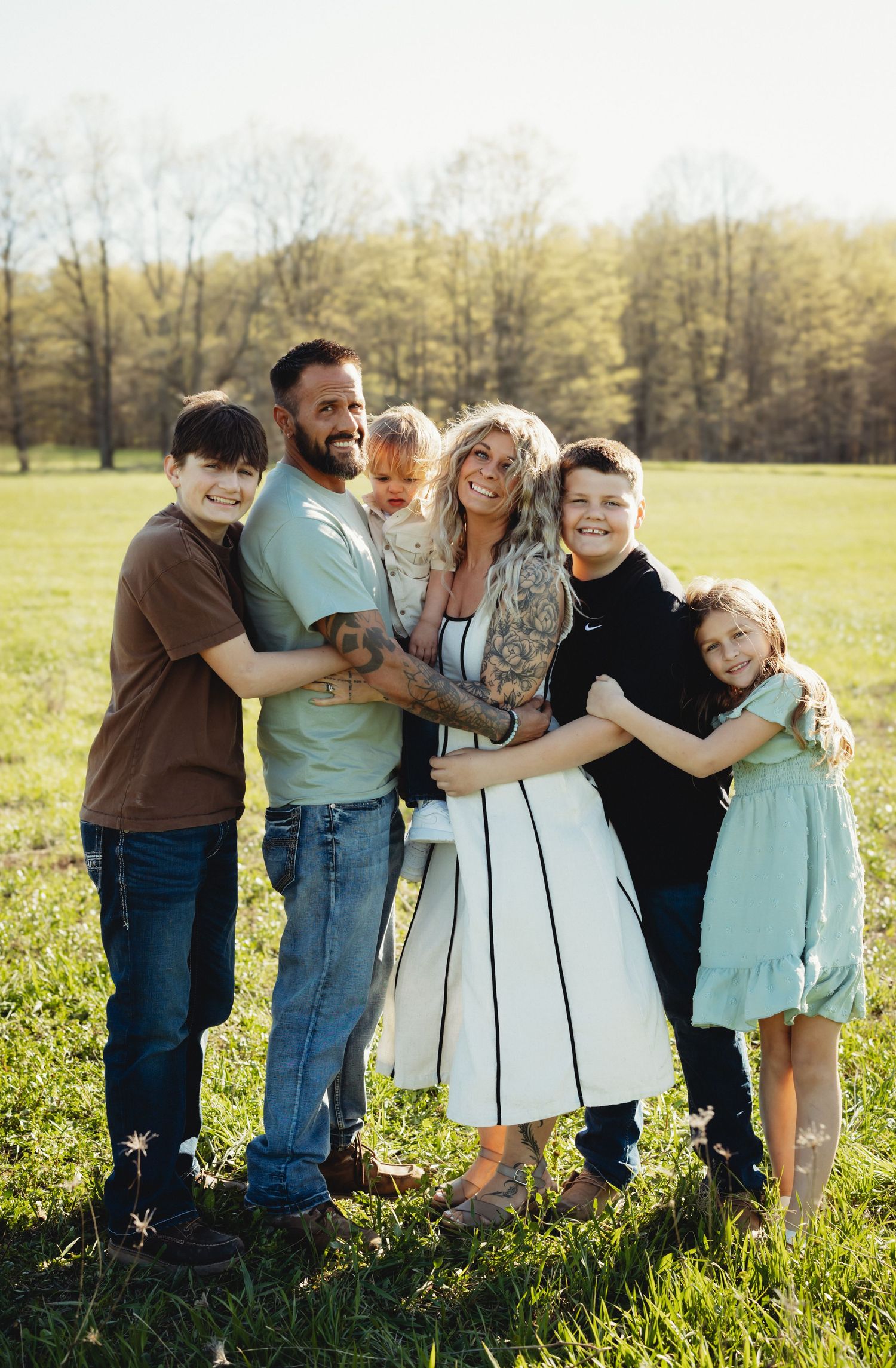 Happy family of six posing outdoors in a green field, smiling together on a sunny spring day.