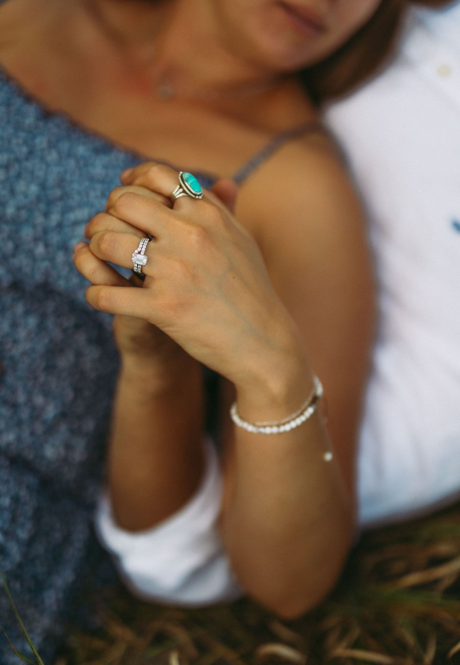 Close-up of a woman's hands adorned with a turquoise ring, diamond band, and pearl bracelet.