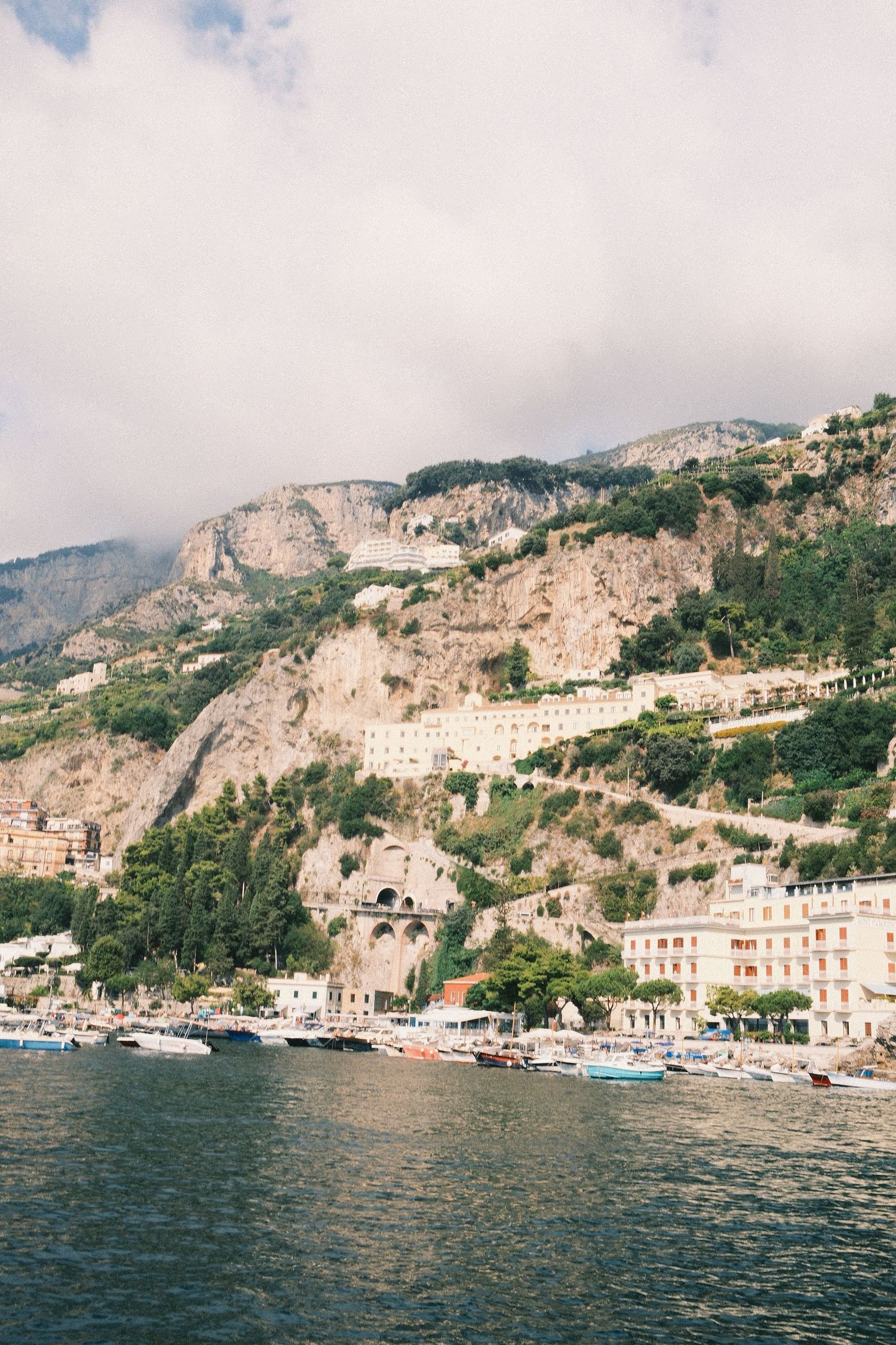 Aerial view of Amalfi Coast town with colorful buildings cascading down rocky cliffs to the Mediterranean Sea.