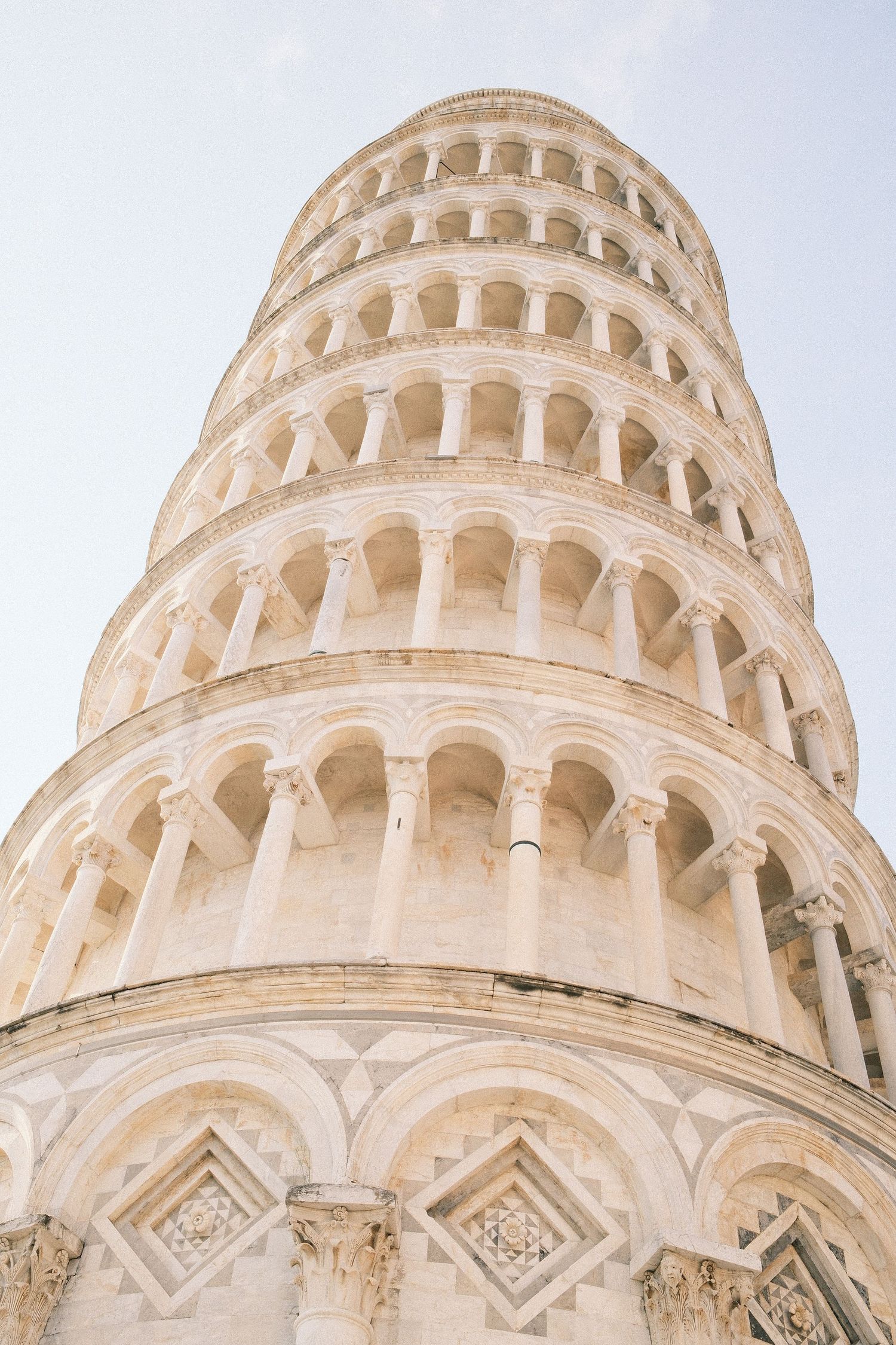 Close-up view of the iconic Leaning Tower of Pisa, showcasing its white marble arches and columns against a clear sky.