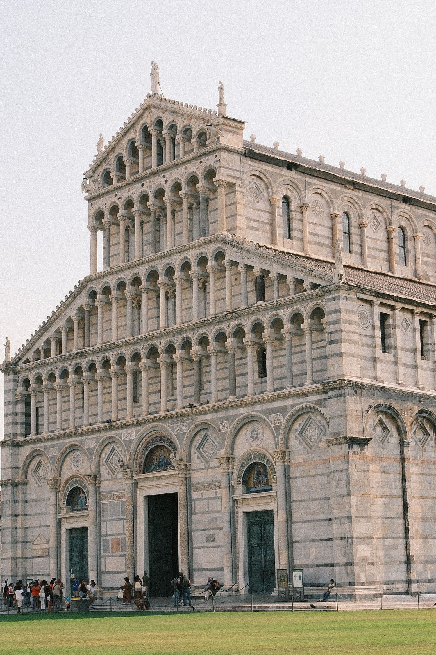 The ornate white marble facade of the Pisa Cathedral in Italy, featuring tiered arches and columns under a clear sky.