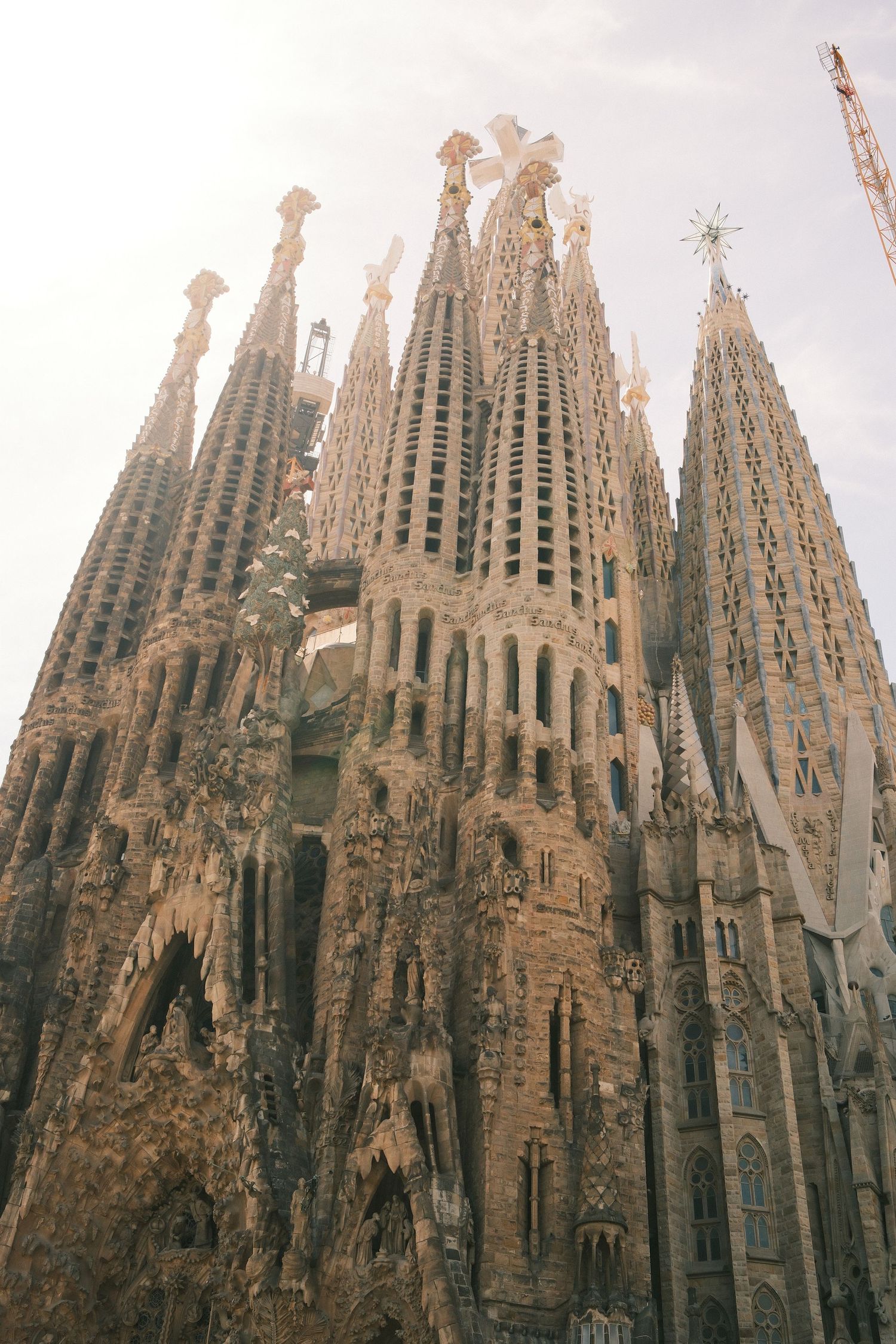 Ornate spires of Sagrada Familia basilica in Barcelona, designed by Antoni Gaudi, against a hazy sky.