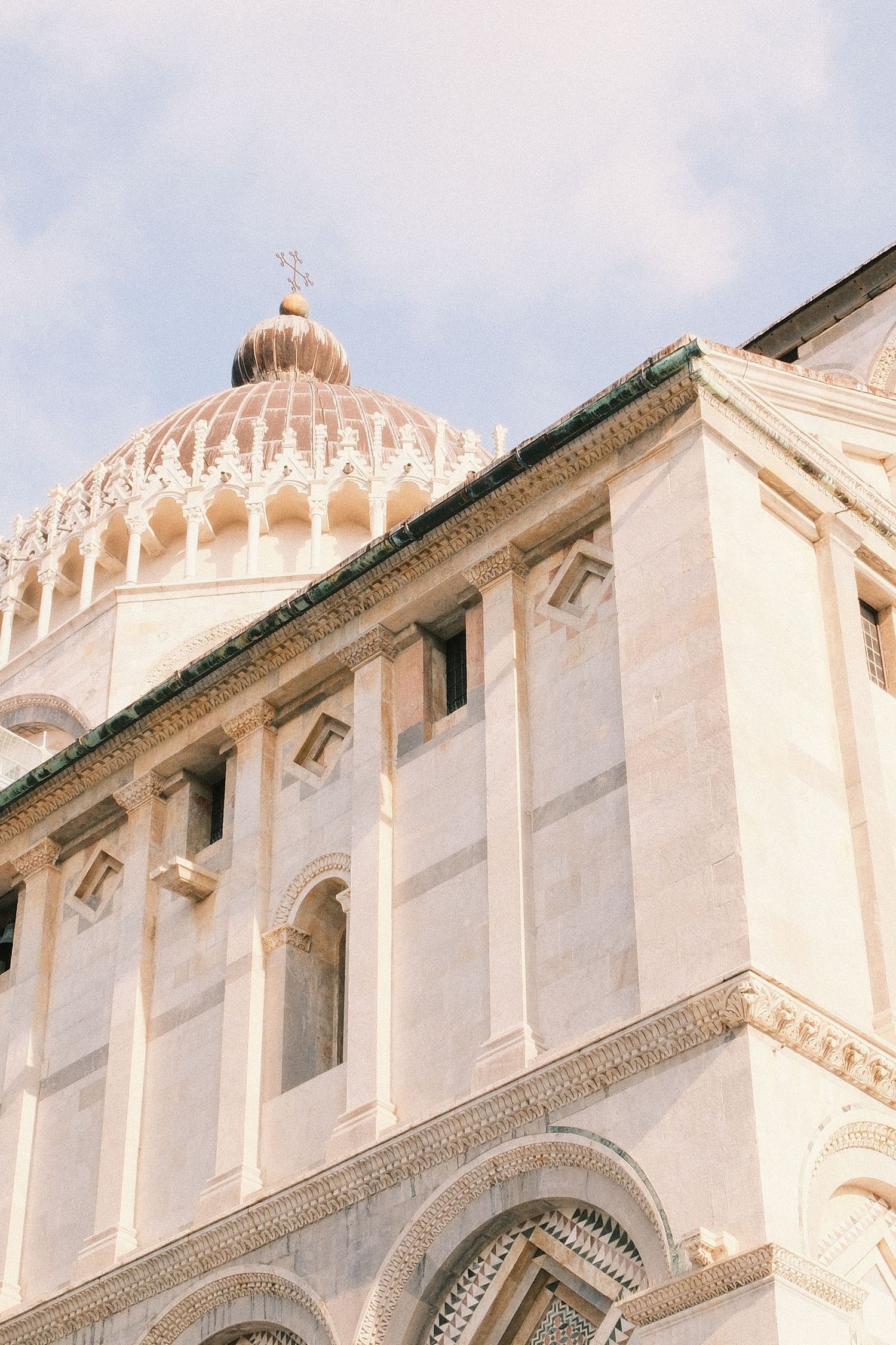 Close-up view of the ornate marble facade and dome with cross of the Pisa Cathedral in Italy.