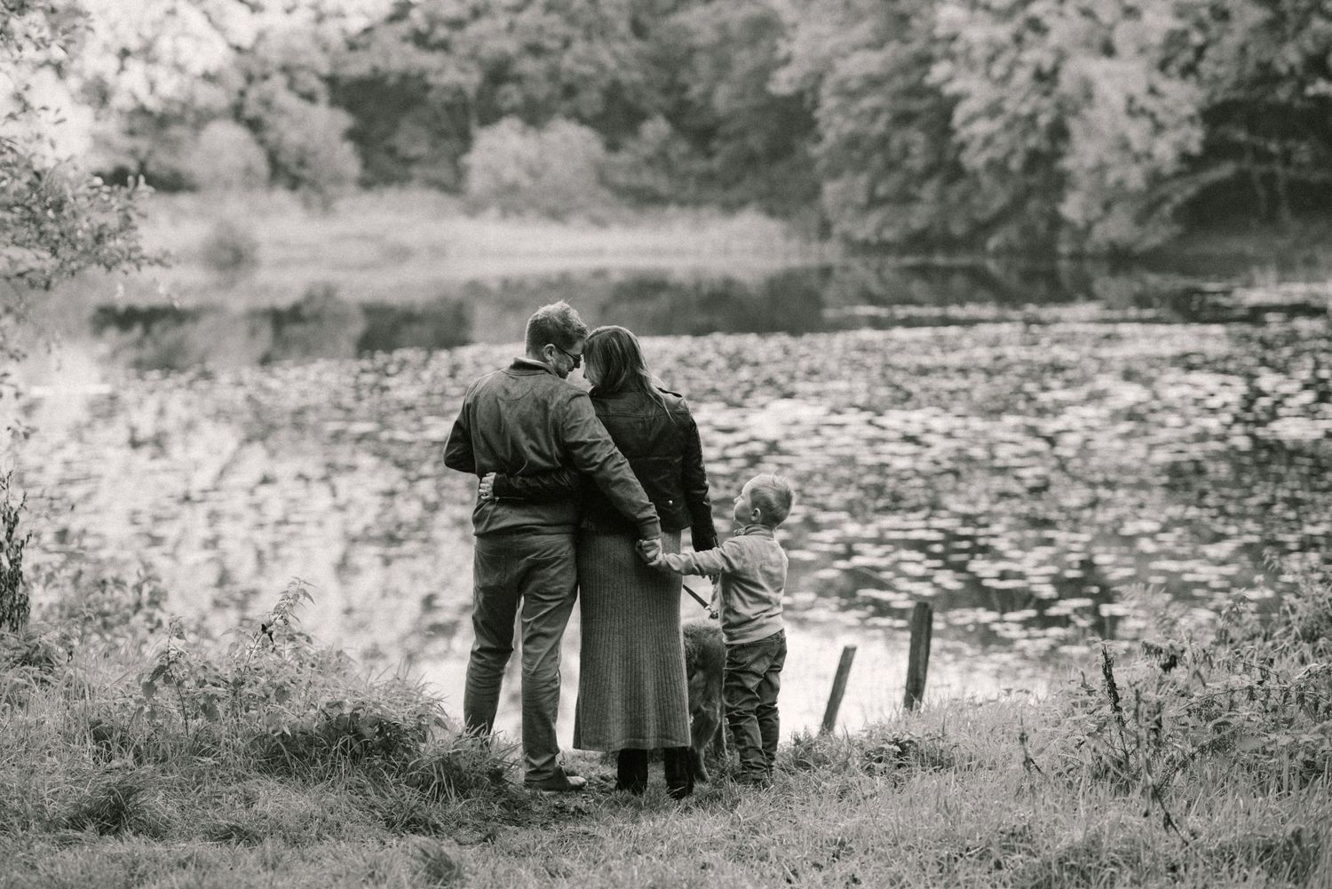 Black and white image of family embracing with a dog by the lake with small boy in Rossmore park Monaghan