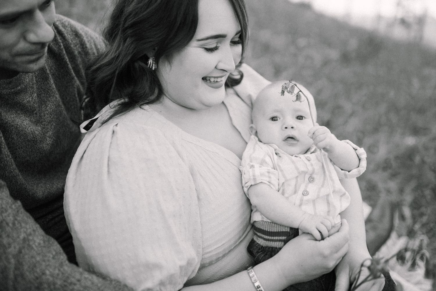 Black and white image of happy family with small baby in a bluebells field