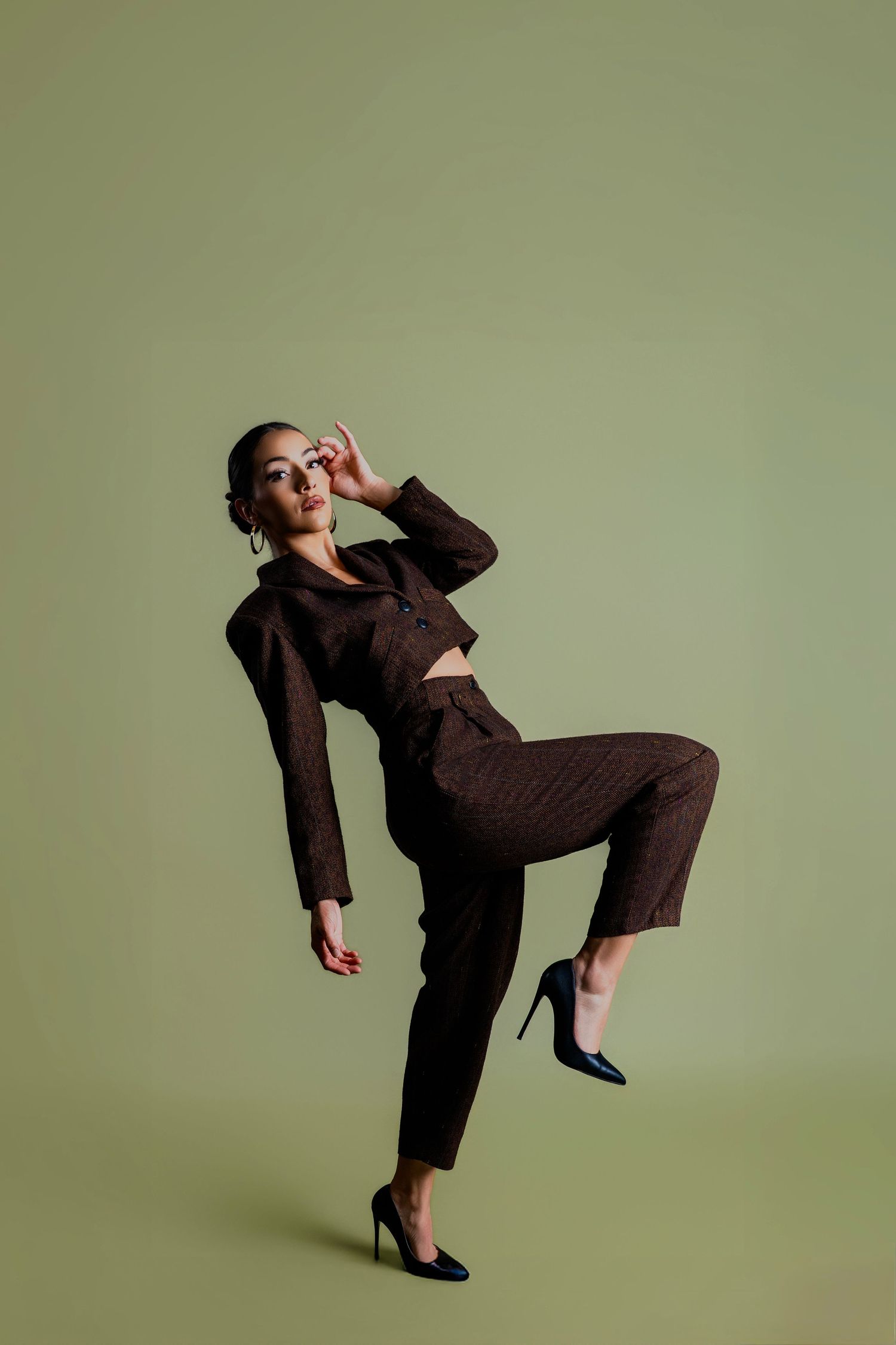 A figure in a brown suit performs dynamic dance poses against a sage green backdrop, creating an artistic movement sequence.