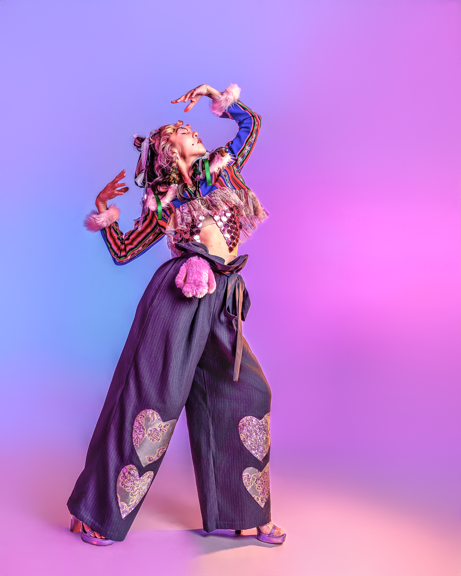 Playful fashion pose showing dark overalls with decorative heart patches in studio setting.