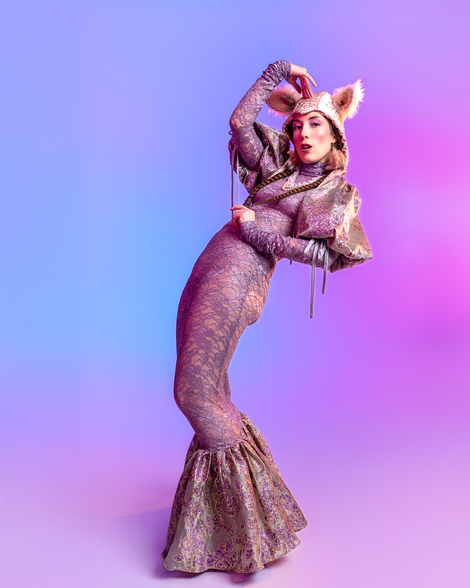 Fashion model in fitted purple gown striking dramatic pose against gradient backdrop.