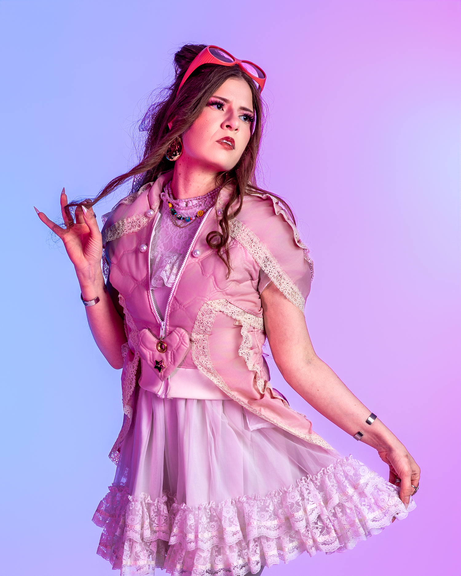 Fashion model in frilly pink dress poses expressively on purple-lit studio set.